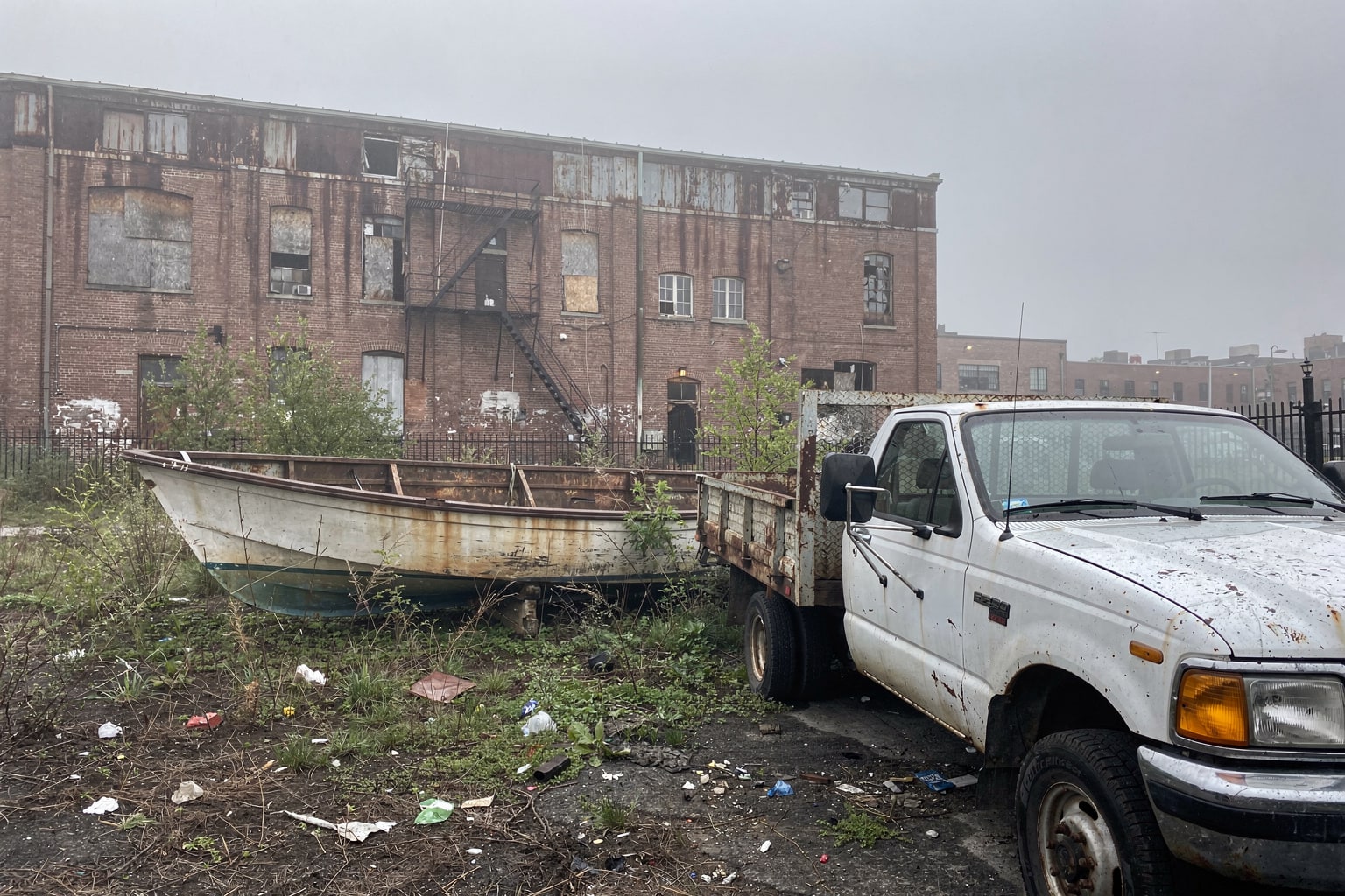 Abandoned sailboat junk boat removal Brooklyn—weathered hull in overgrown yard with pickup truck approaching