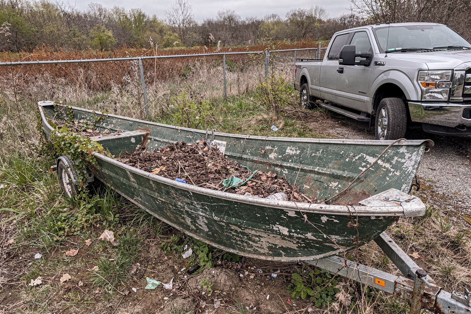 Abandoned junk boat on bare ground surrounded by weeds in Colorado Springs yard, trailer positioned for boat removal