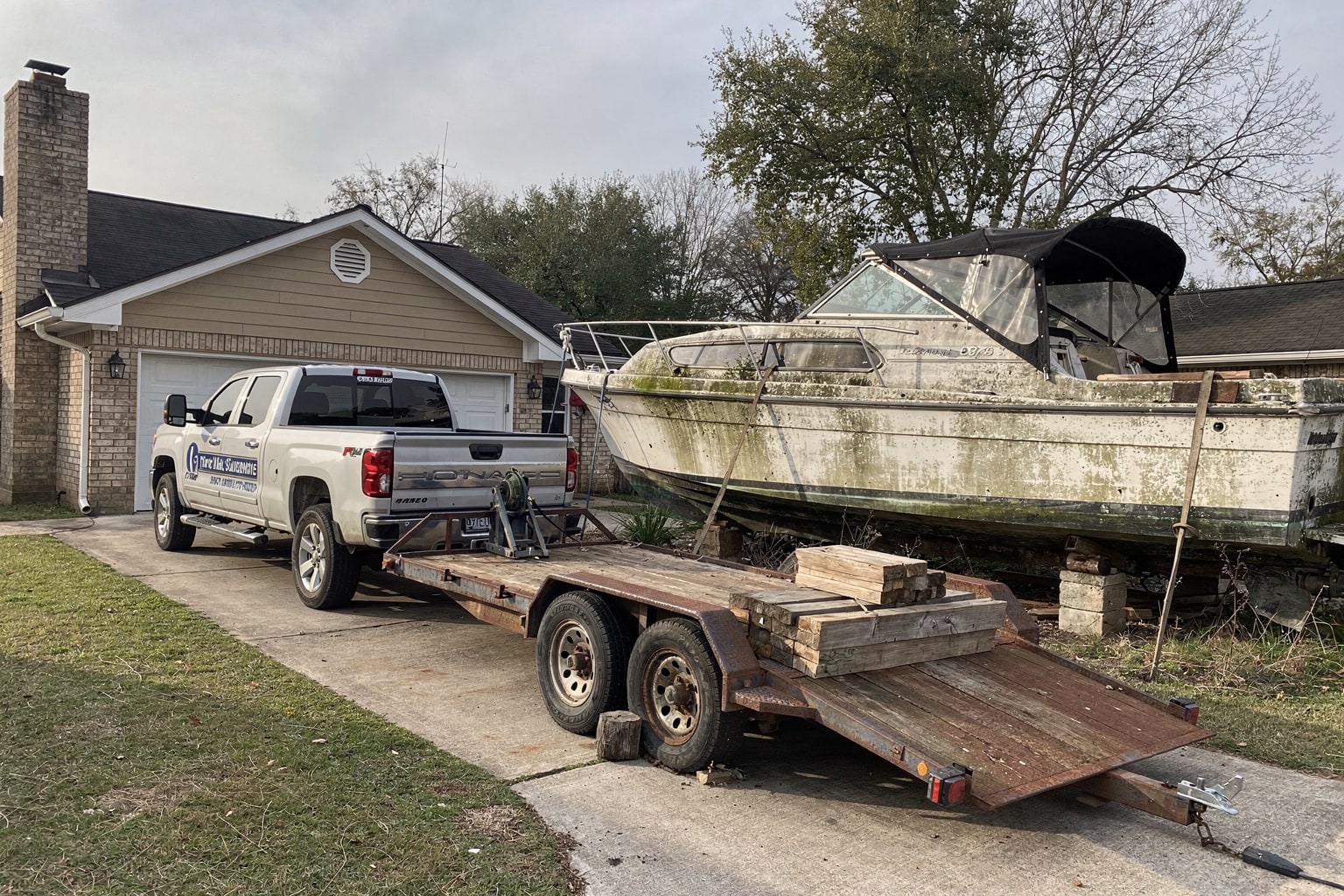 Abandoned deteriorating cabin cruiser boat removal Houston on rotted blocks surrounded by weeds and debris requiring professional disposal