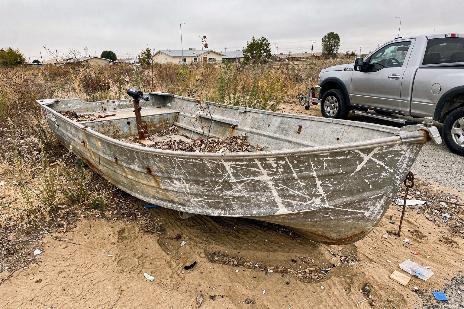 Junk boat removal Bakersfield CA abandoned weathered aluminum fishing boat overgrown yard