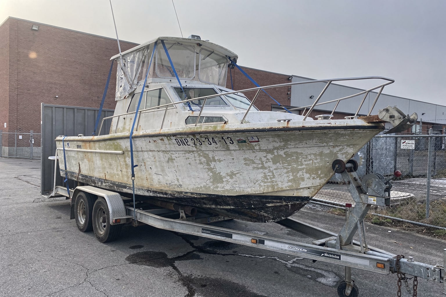 Boat removal and disposal Brookhaven NY — 28-foot cabin cruiser on hydraulic trailer at industrial lot with flatbed truck