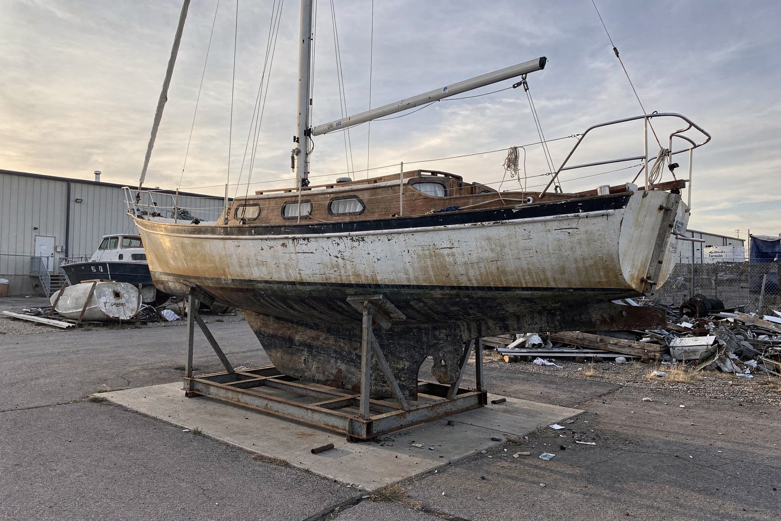 Boat disposal Denver CO — weathered sailboat on cradle at commercial yard with other junk boats visible