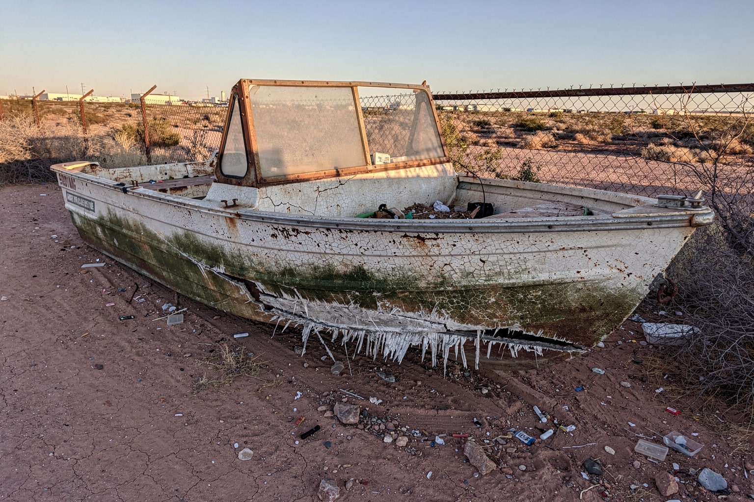 Severely damaged junk jon boat on bare ground, El Paso boat disposal service, abandoned fiberglass