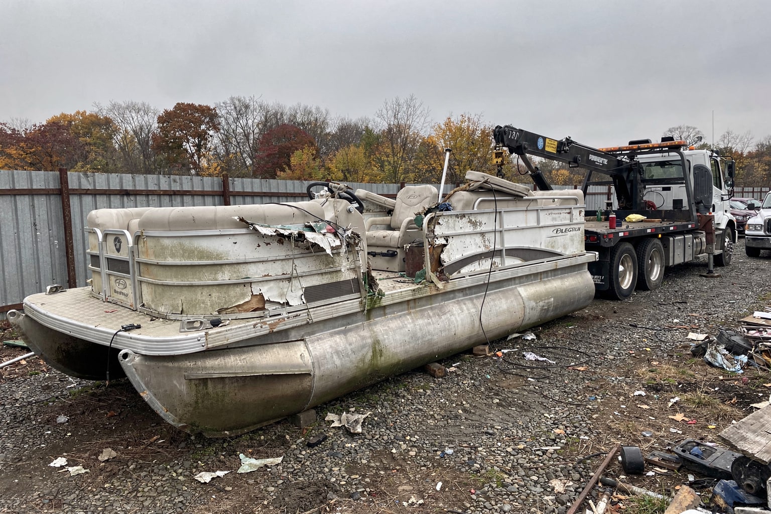 Damaged pontoon junk boat on salvage yard ground with tow truck staged for removal and disposal in Louisville Kentucky