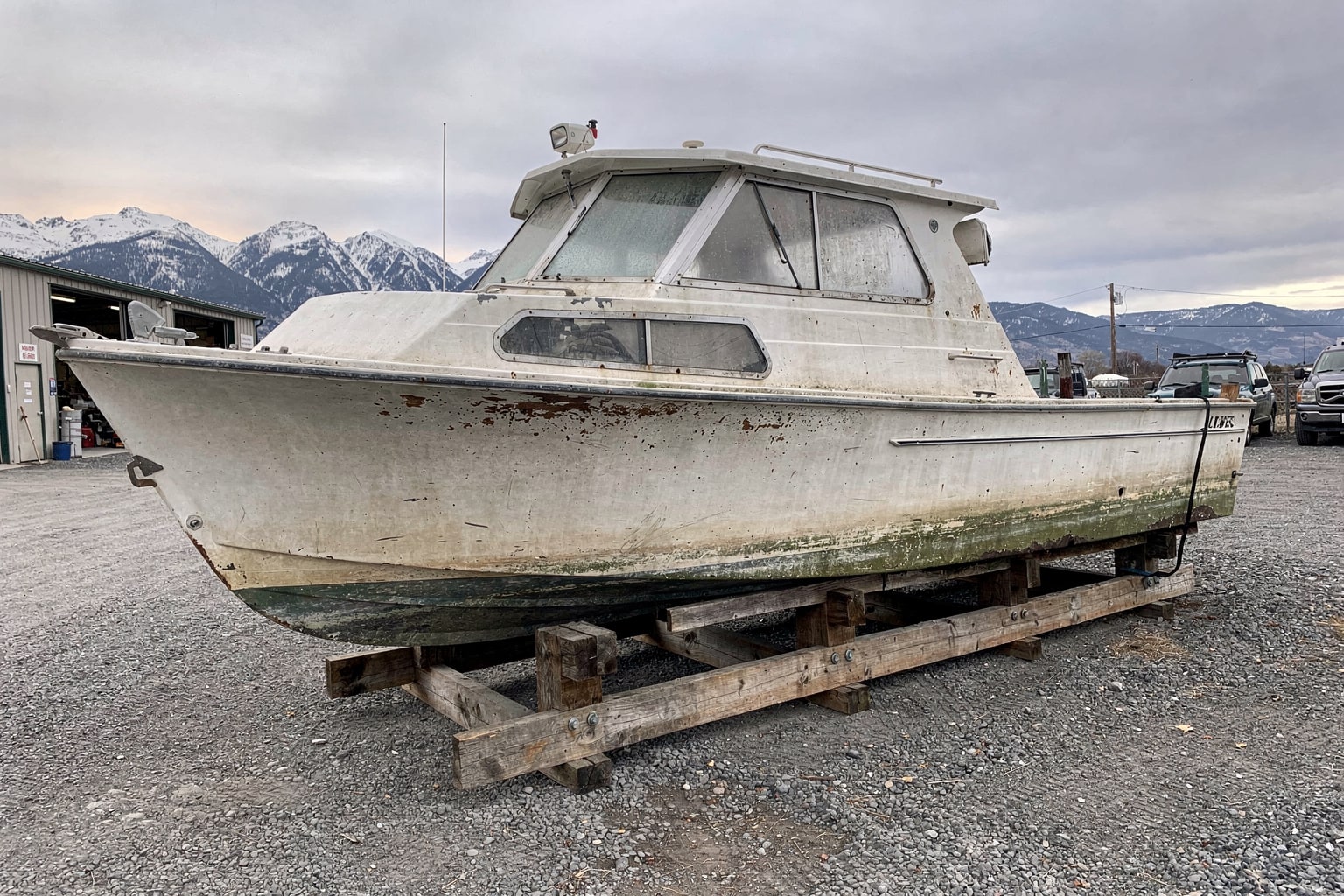 Boat disposal Montana — deteriorated fiberglass cabin cruiser on cradle blocks in salvage storage yard, ready for removal