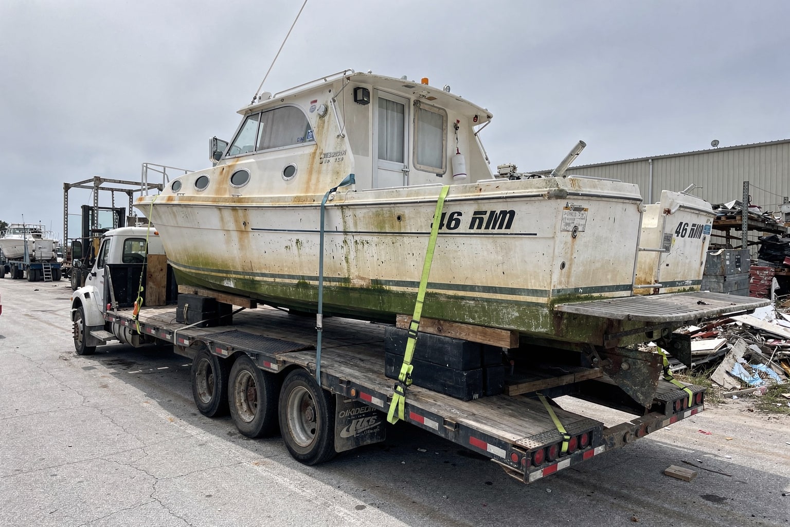 Boat removal Alabama commercial salvage: cabin cruiser on flatbed truck at marine salvage yard