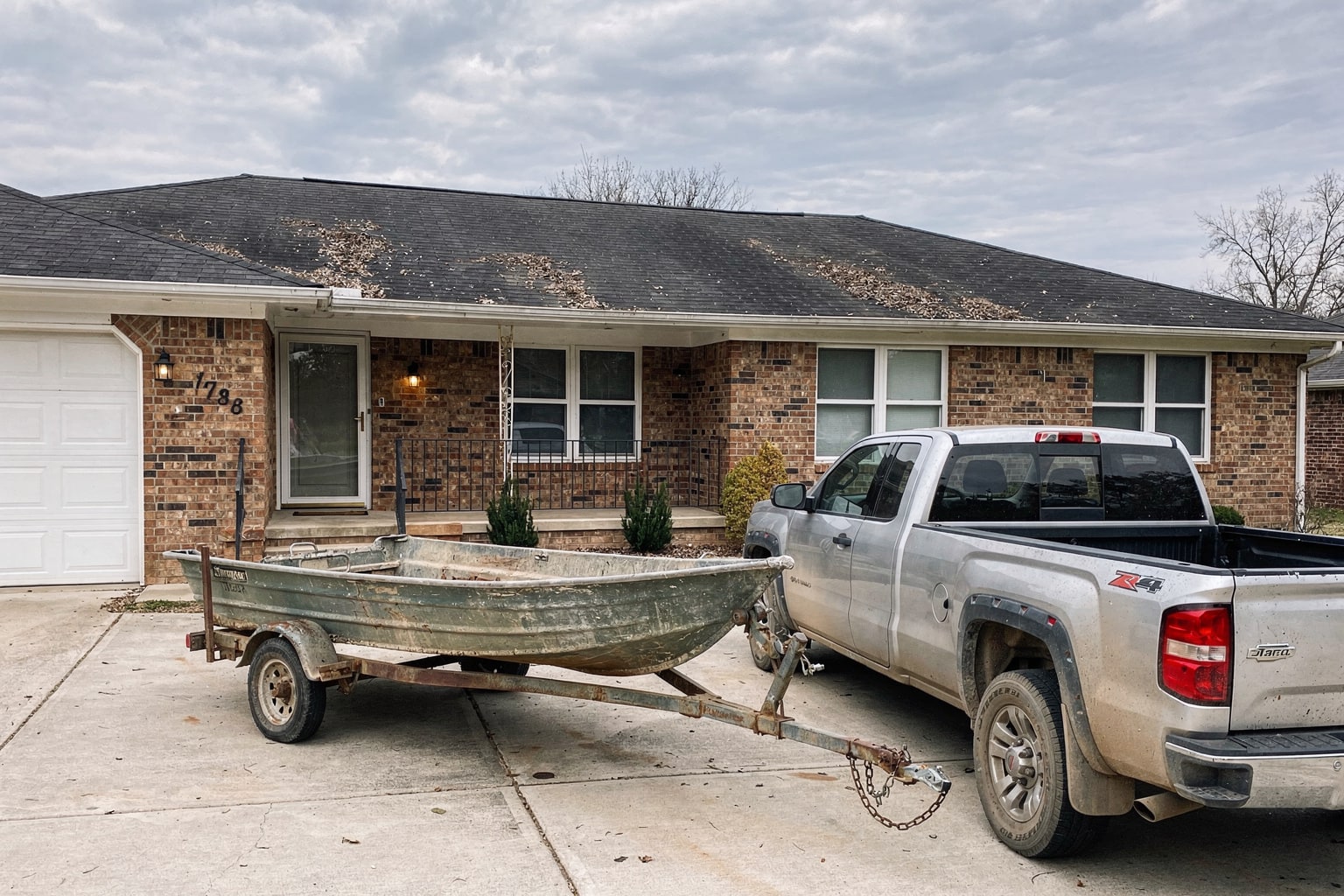 Junk boat removal in Arkansas: weathered fishing boat on trailer attached to pickup truck in residential driveway
