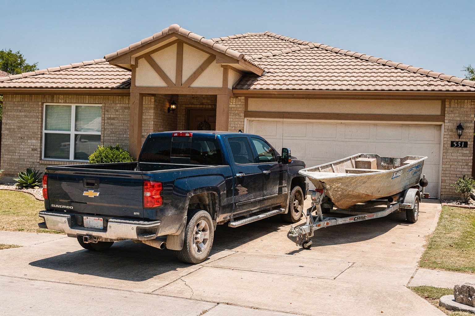 Junk boat removal Austin TX: weathered fiberglass powerboat loaded on trailer behind pickup truck in residential driveway