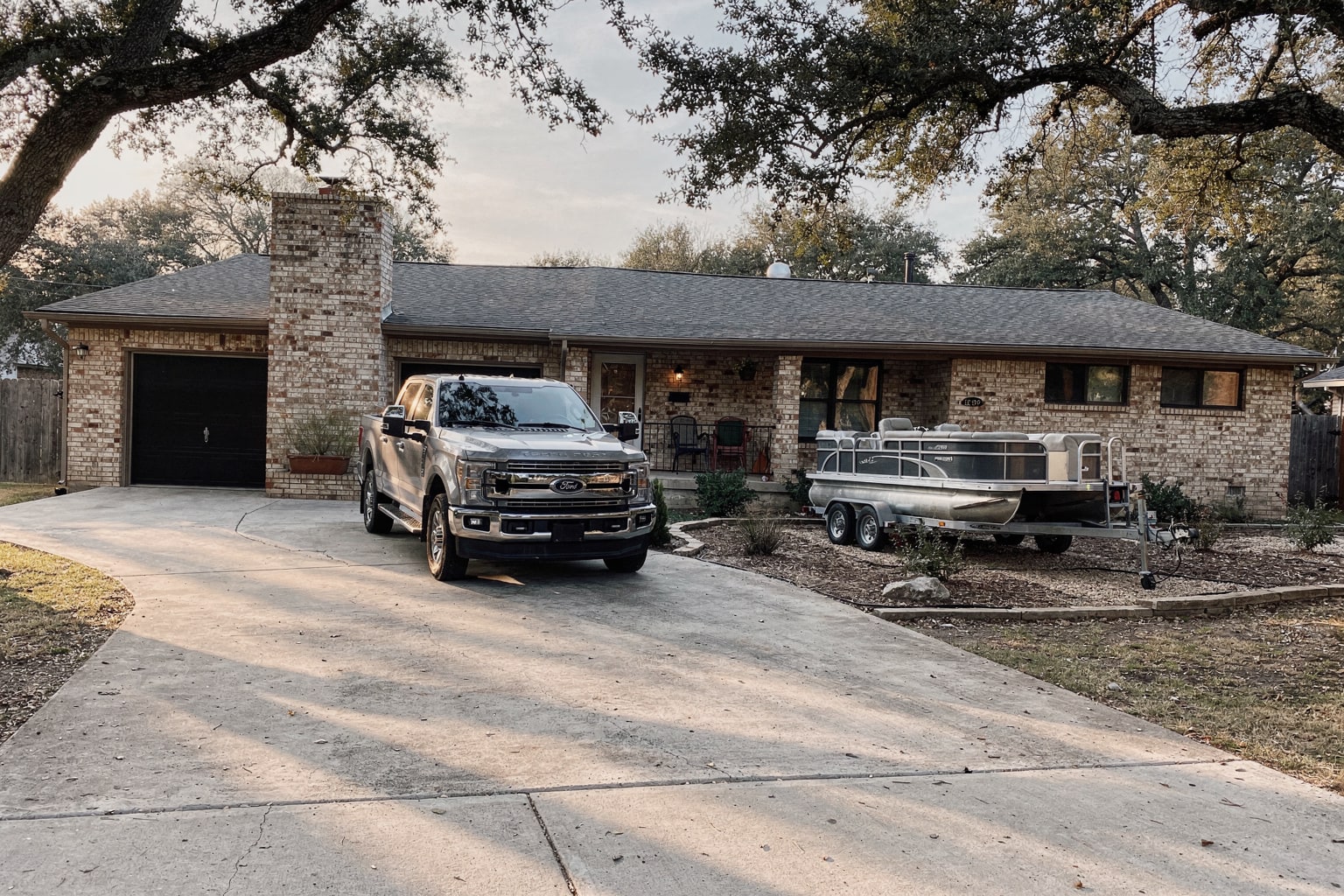 Boat disposal service Austin: rusty pontoon boat removal on tandem-axle trailer parked at residential home