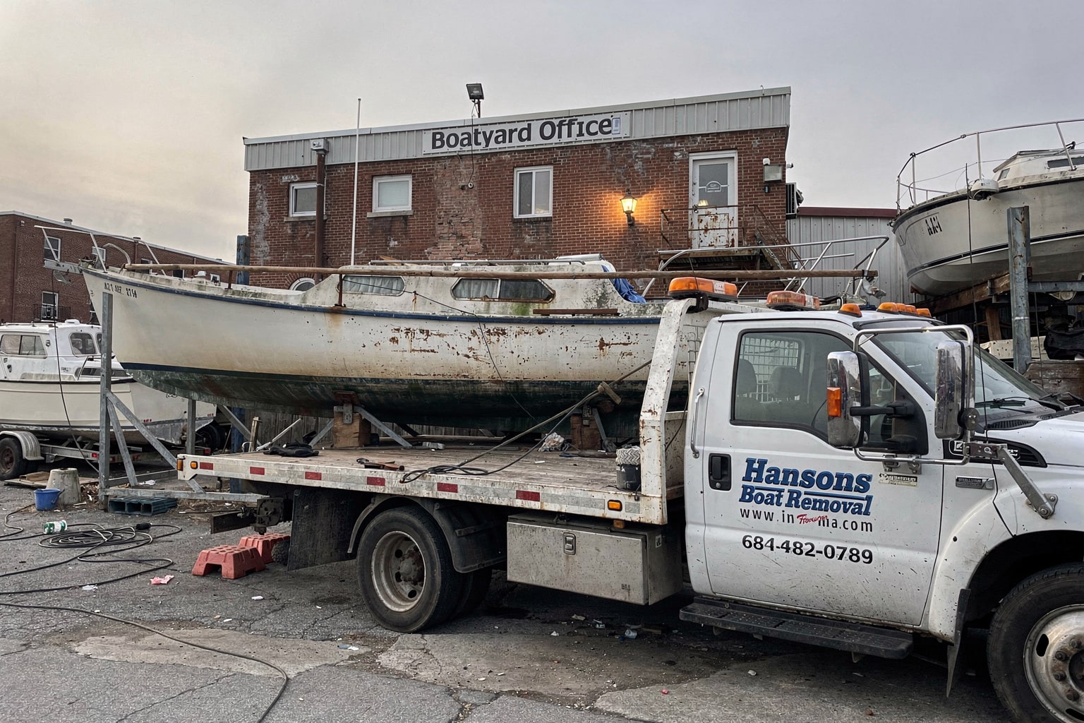 Abandoned 28-foot sailboat on cradle at Baltimore boatyard with multiple junk boats awaiting removal and disposal service