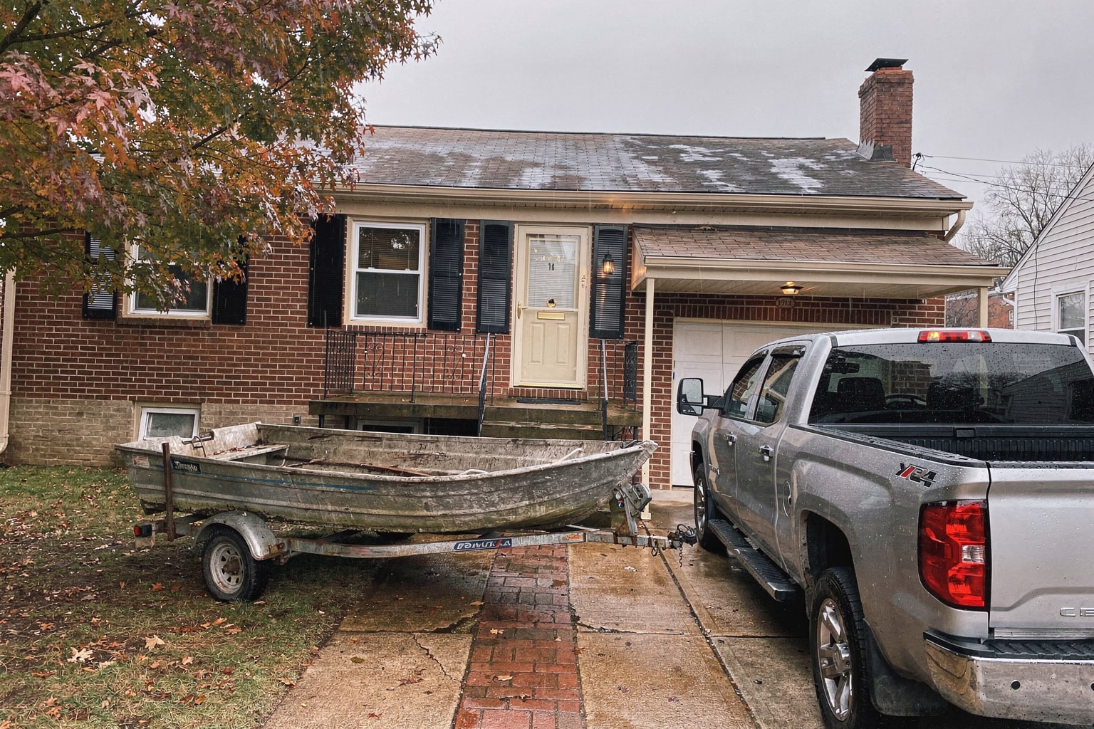 Junk boat removal service in Baltimore with deteriorated aluminum fishing boat loaded on trailer behind pickup truck in residential driveway