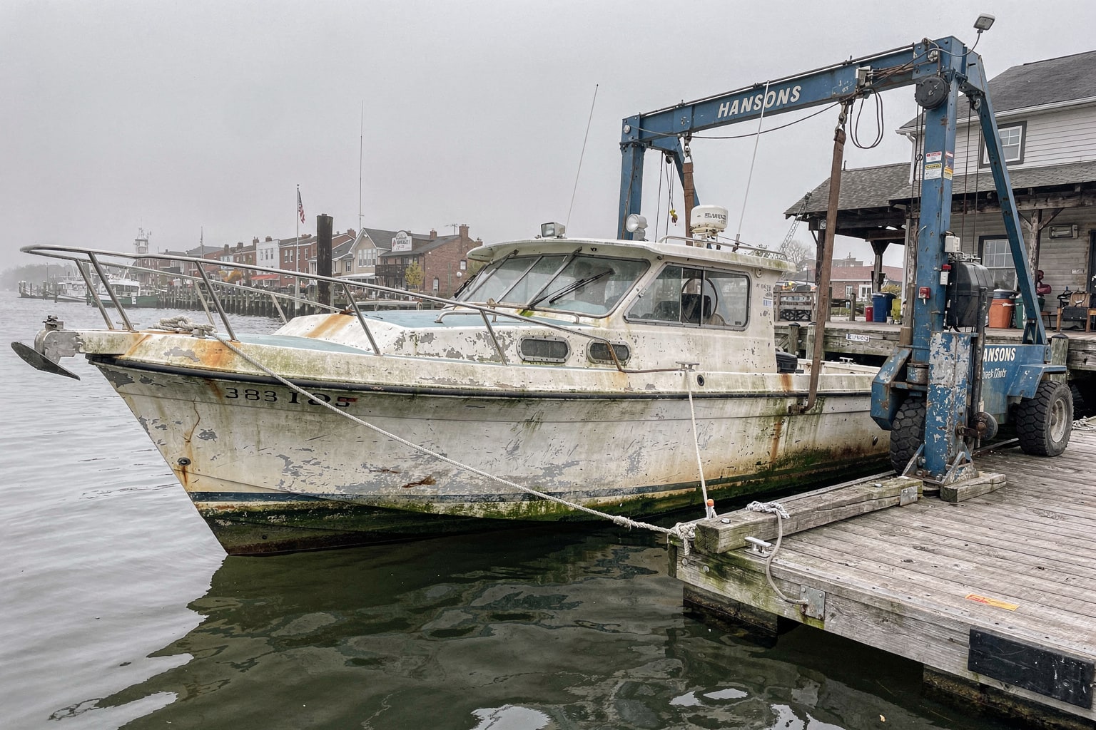 Neglected 22-foot powerboat ready for junk boat disposal at Baltimore harbor marina dock with weathered pilings and industrial waterfront
