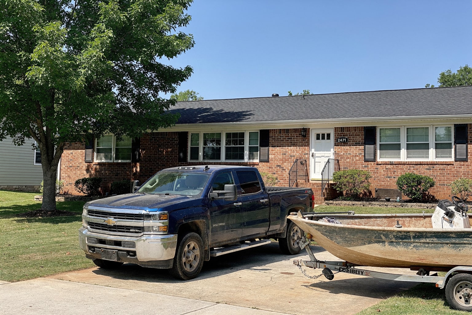 Dark blue pickup truck removing faded blue center console boat on trailer from Charlotte residential driveway