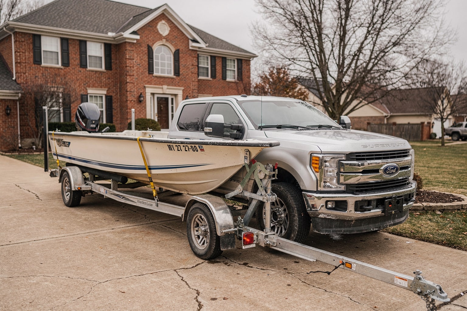 Silver pickup truck hauling fiberglass boat on trailer in Chicago driveway, junk boat removal service