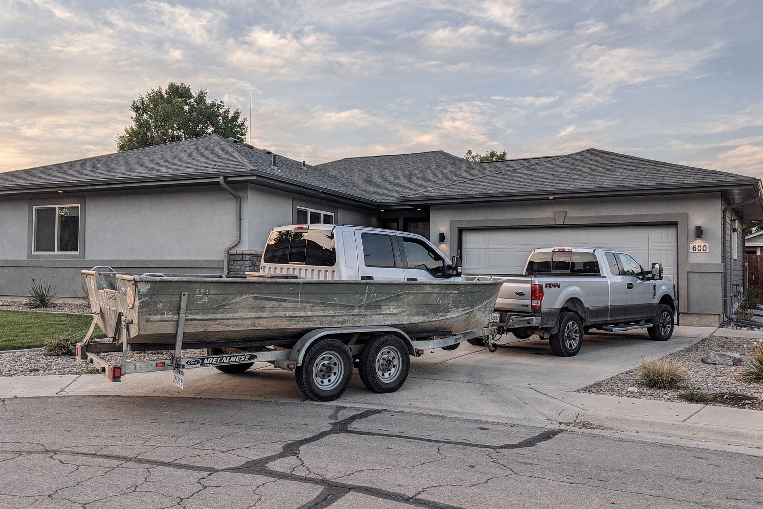 Weathered fishing boat on trailer beside Colorado home ready for removal and salvage