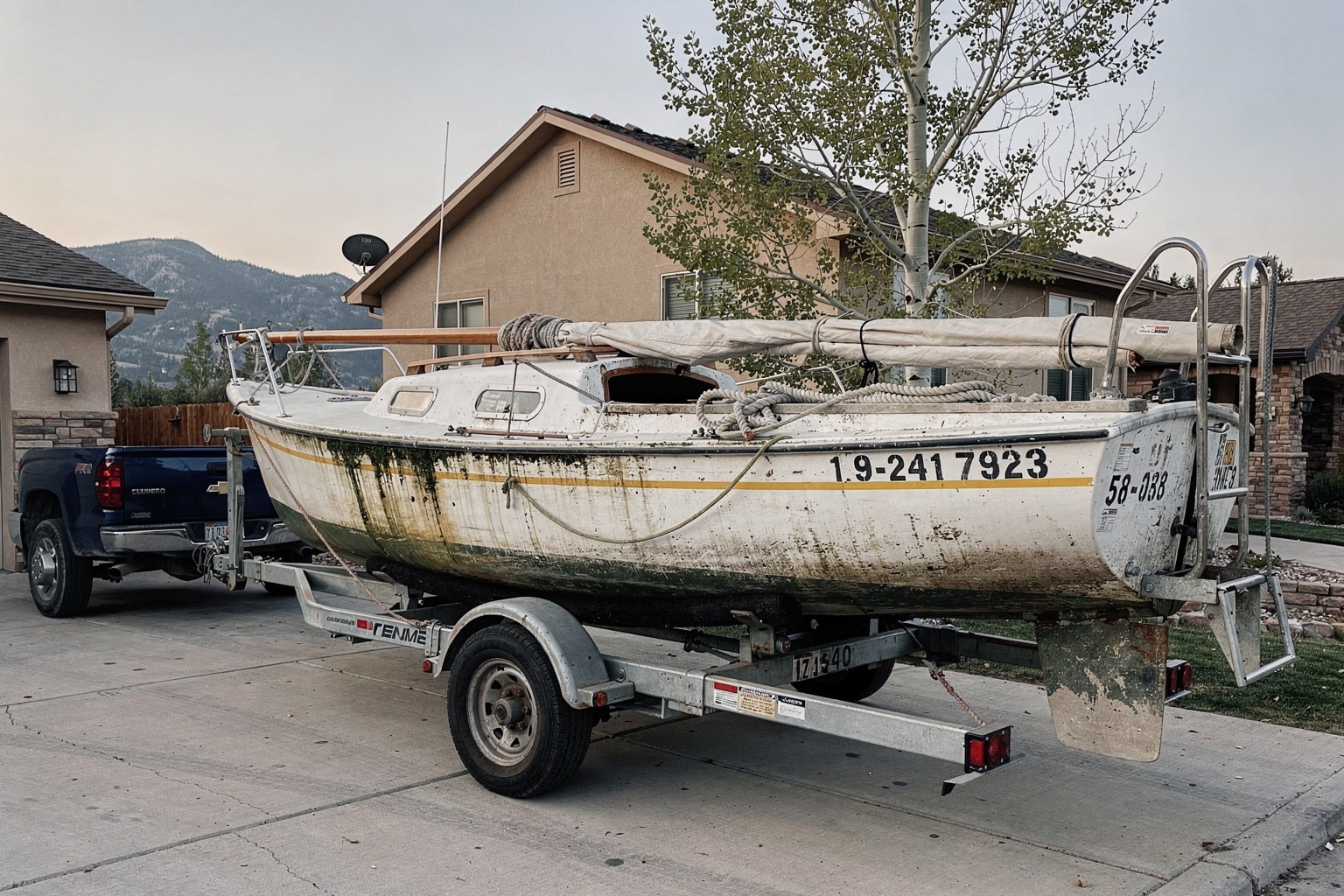 Marine salvage boat removal Colorado residential driveway with weathered sailboat and pickup truck