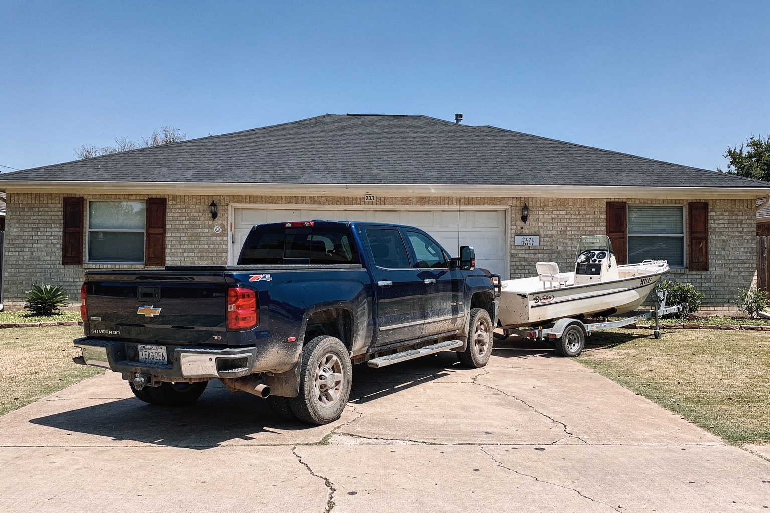 Junk fishing boat removal Dallas Texas on tandem-axle trailer behind dark blue Chevy pickup truck in residential driveway
