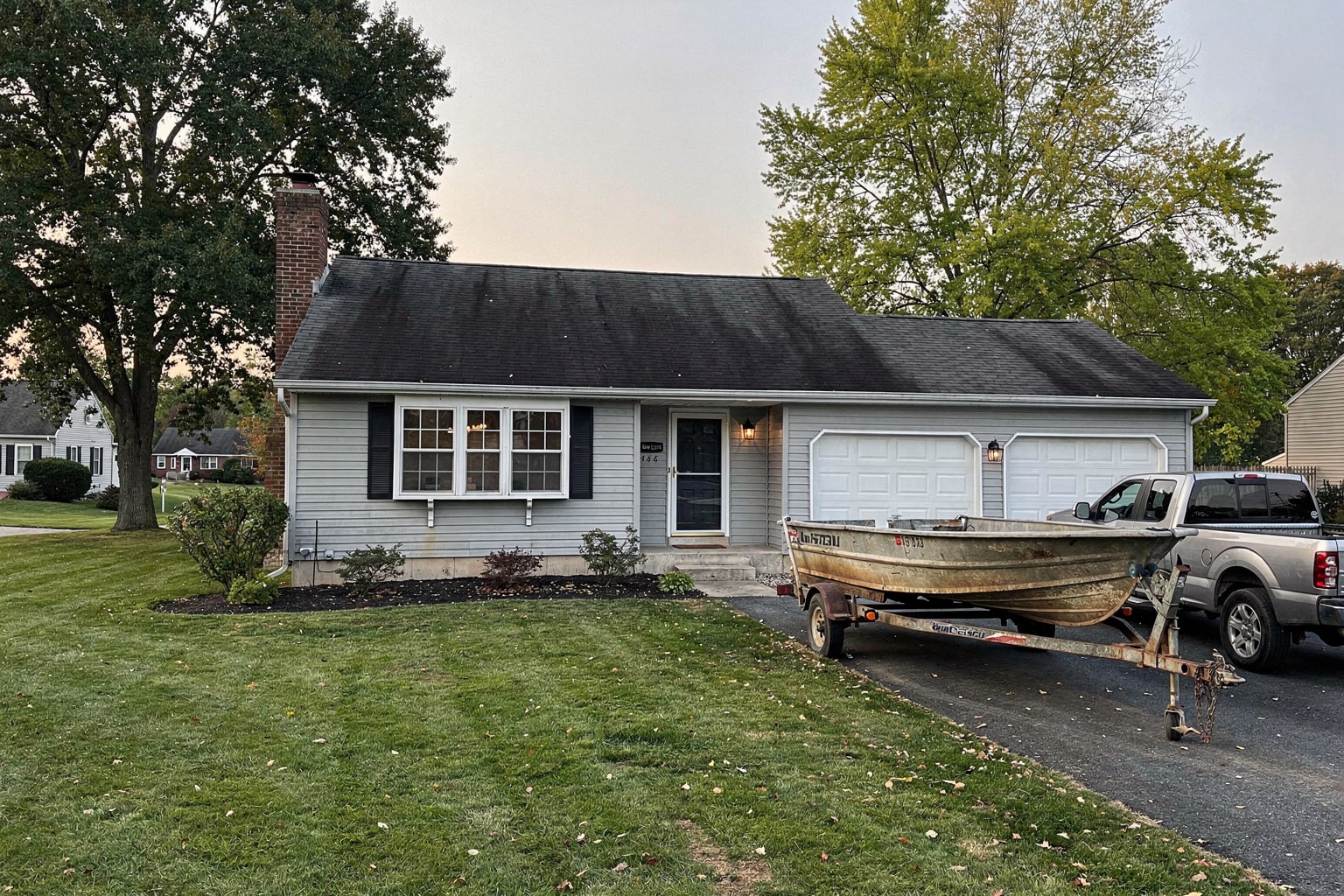 Weathered 16-foot fiberglass boat removal on trailer behind pickup truck in Delaware residential driveway