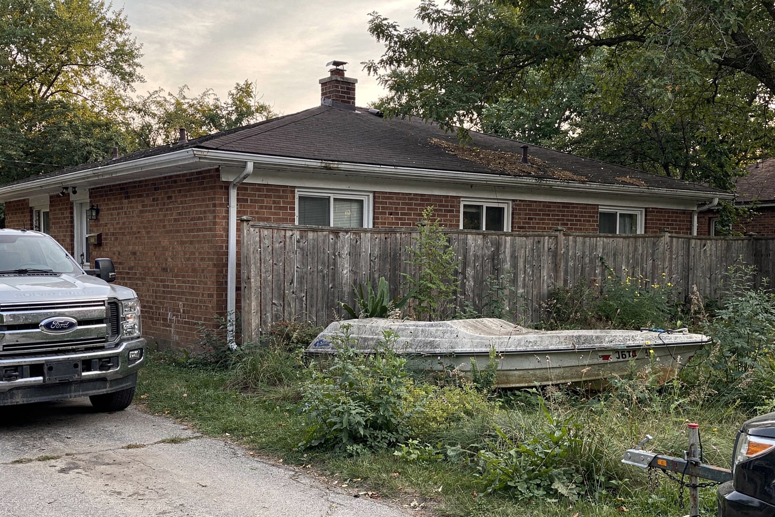 Junk boat disposal in Detroit Michigan showing abandoned aluminum jon boat surrounded by overgrown weeds and deteriorating fence