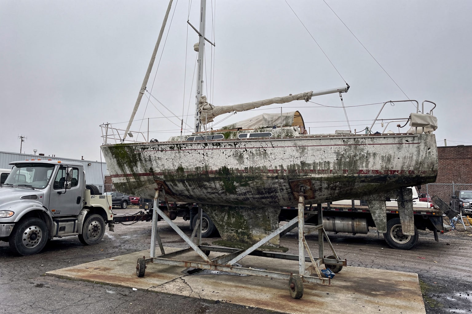 Boat disposal at Detroit boatyard showing large neglected sailboat on steel cradle with other cradled vessels in storage yard