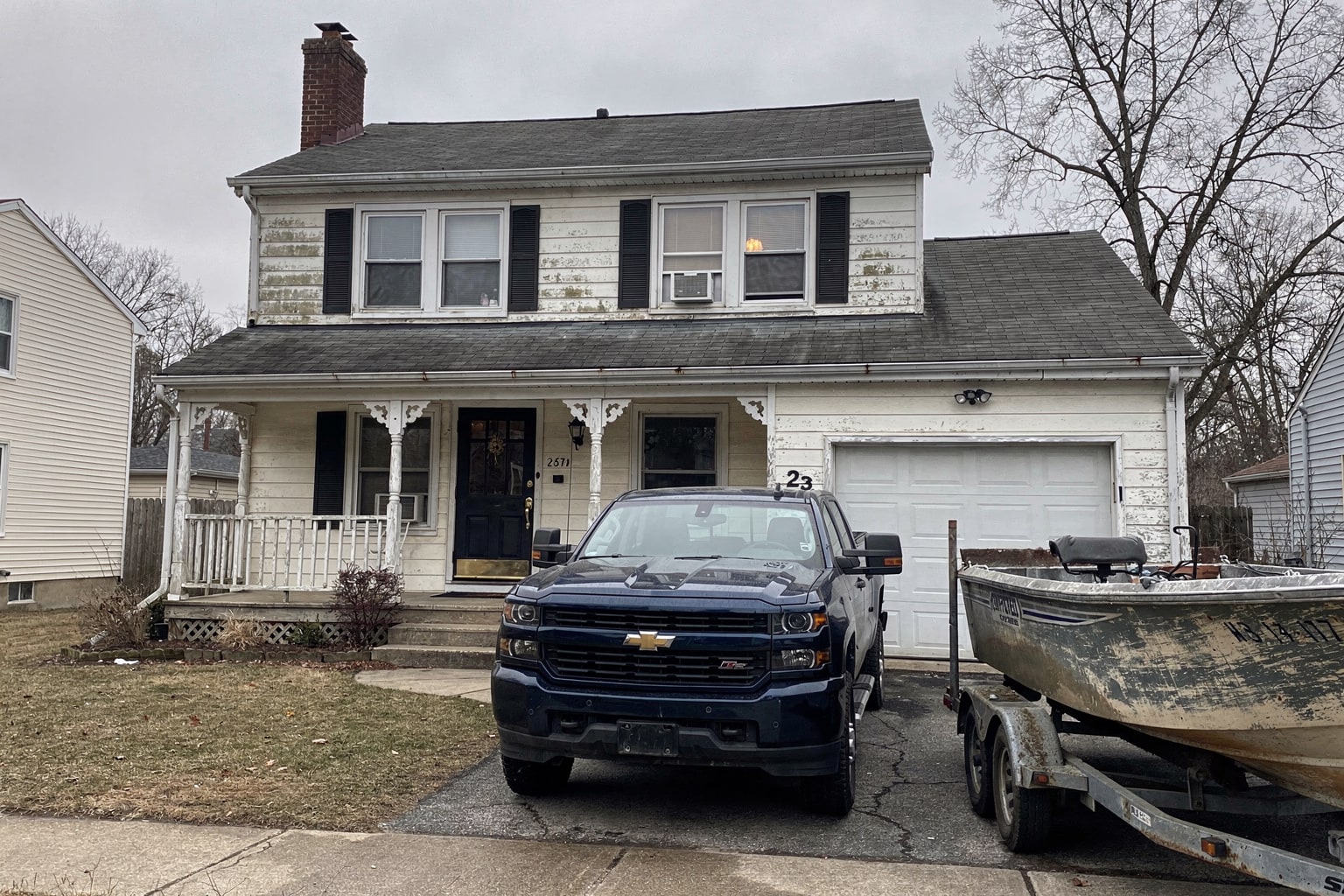Junk boat removal in Detroit showing weathered powerboat loaded on trailer hitched to pickup truck in residential driveway