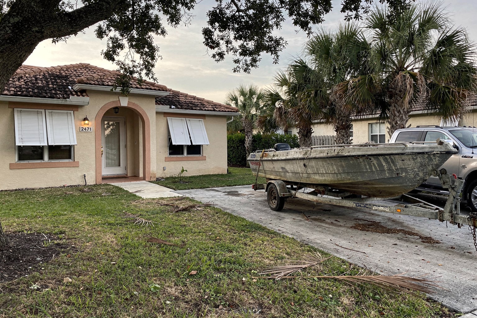 Silver Ford F-250 pickup truck with boat trailer carrying weathered 22-foot powerboat on residential Florida driveway with palm trees and stucco home in background