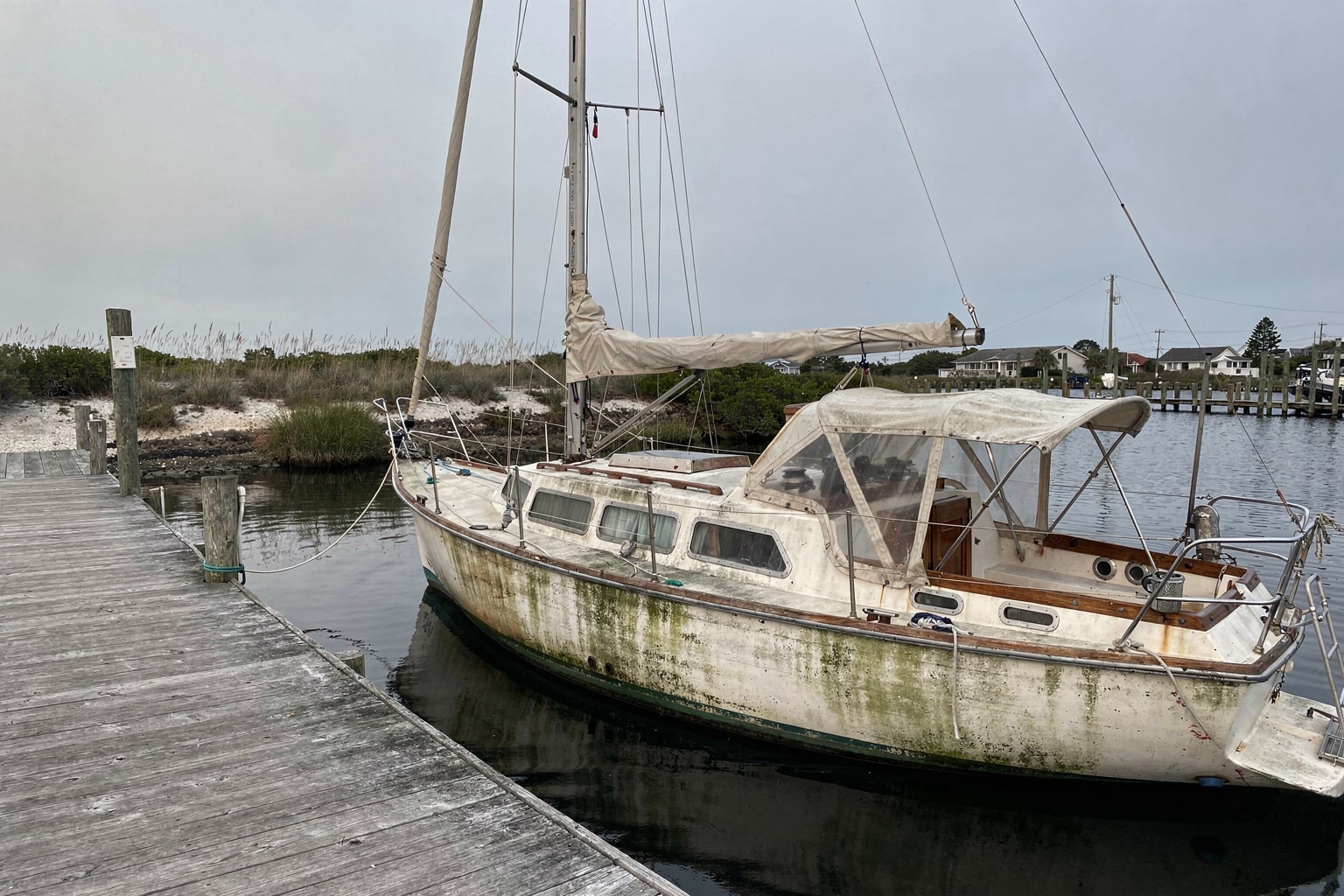 Abandoned 28-foot sailboat with severe algae and rust at deteriorated Florida marina with weathered pier and dockhouse, marine salvage removal service