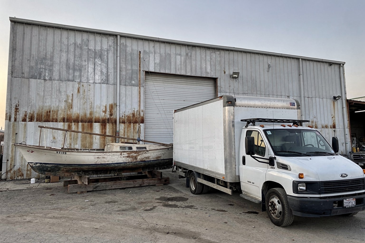 Junk boat disposal Fresno California, abandoned sailboat staged at commercial yard with box truck and dumpster for removal
