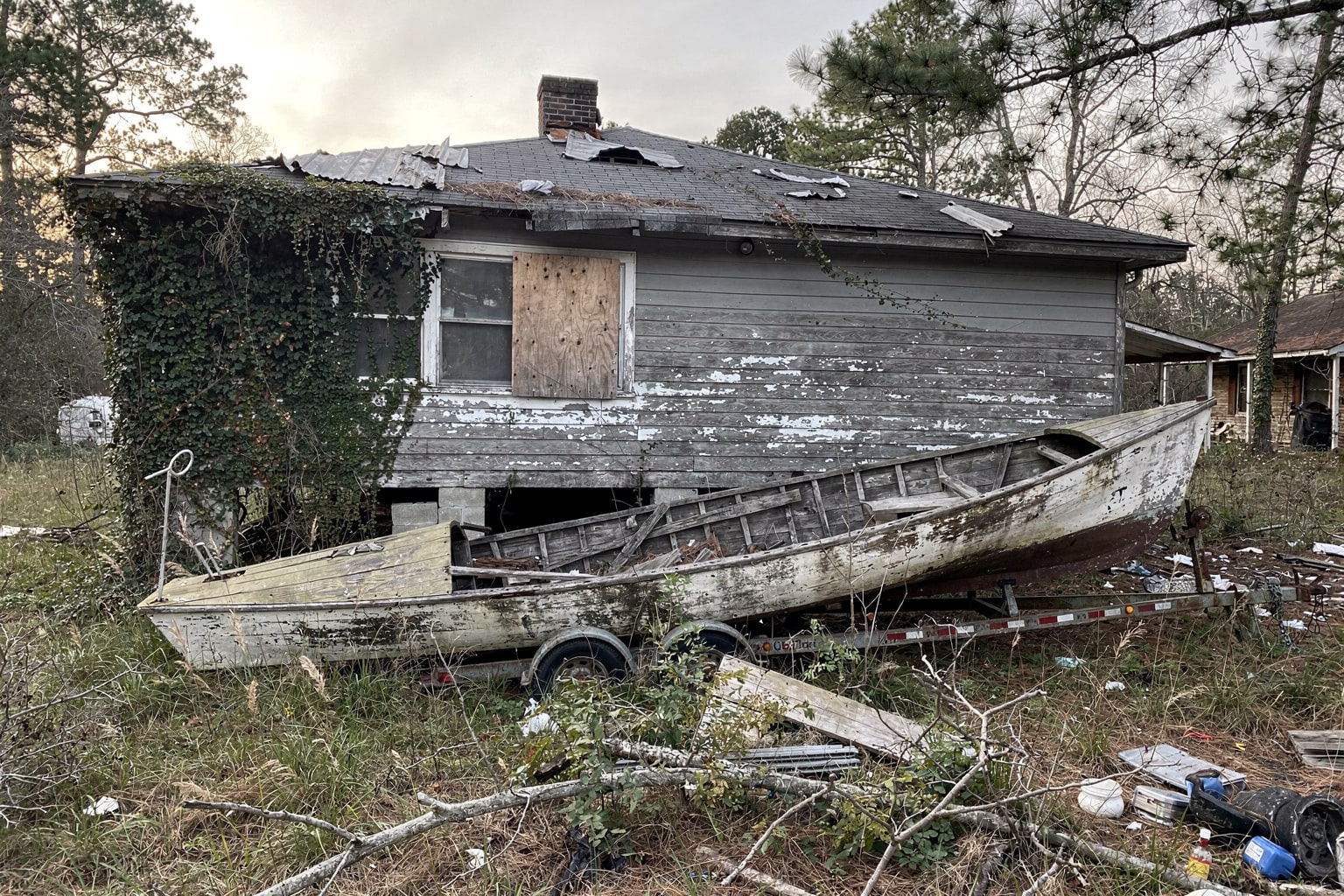 Abandoned derelict wooden sailboat salvage removal in overgrown Georgia property with junk debris and deteriorated hull.