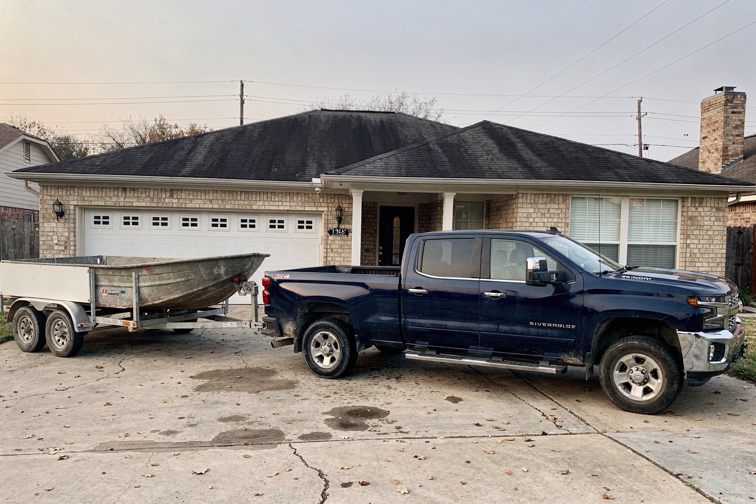 Junk boat removal Houston shows weathered fishing boat loaded on trailer behind pickup truck in residential driveway