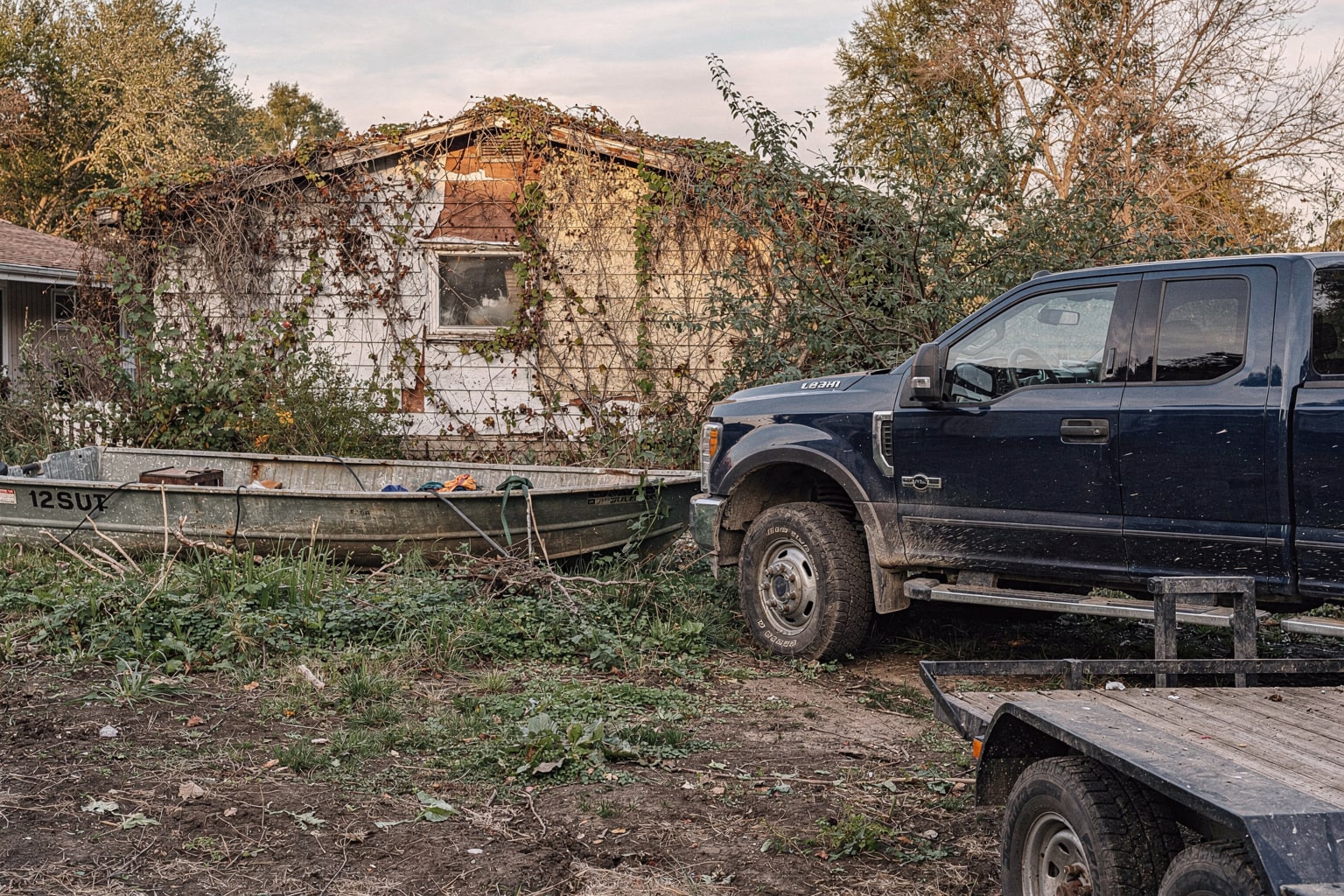Abandoned jon boat removal from overgrown Illinois backyard, pickup truck and empty trailer staged nearby