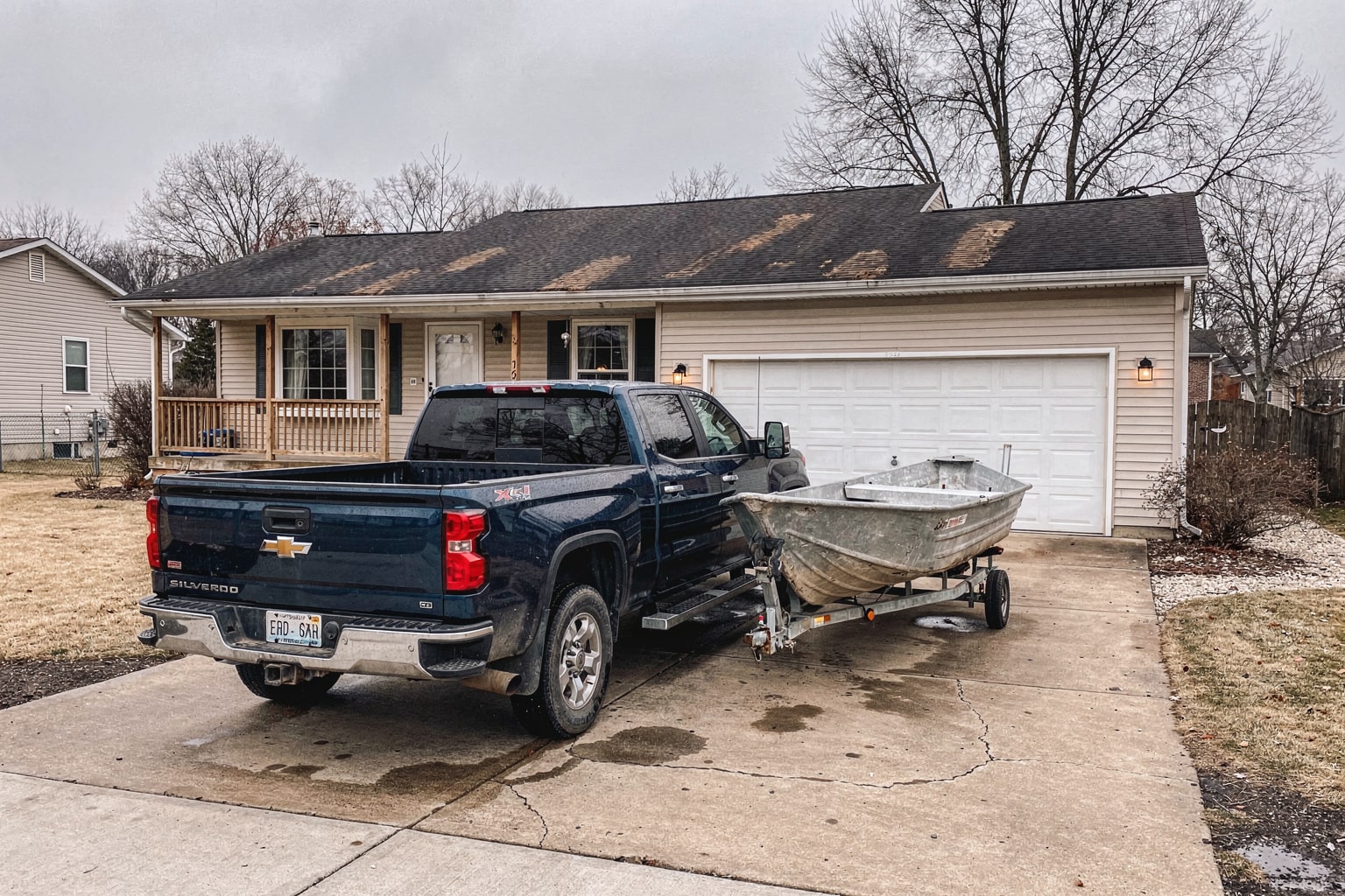 Weathered aluminum fishing boat loaded on trailer behind pickup truck in Illinois residential driveway removal service