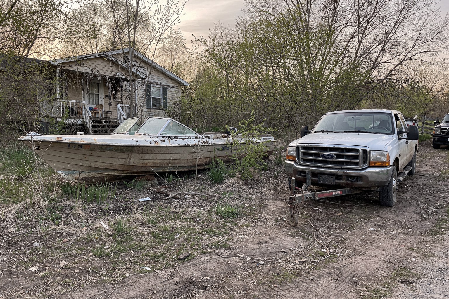 Abandoned junk boat removal from overgrown Indiana property, weathered hull surrounded by weeds and deteriorating fence