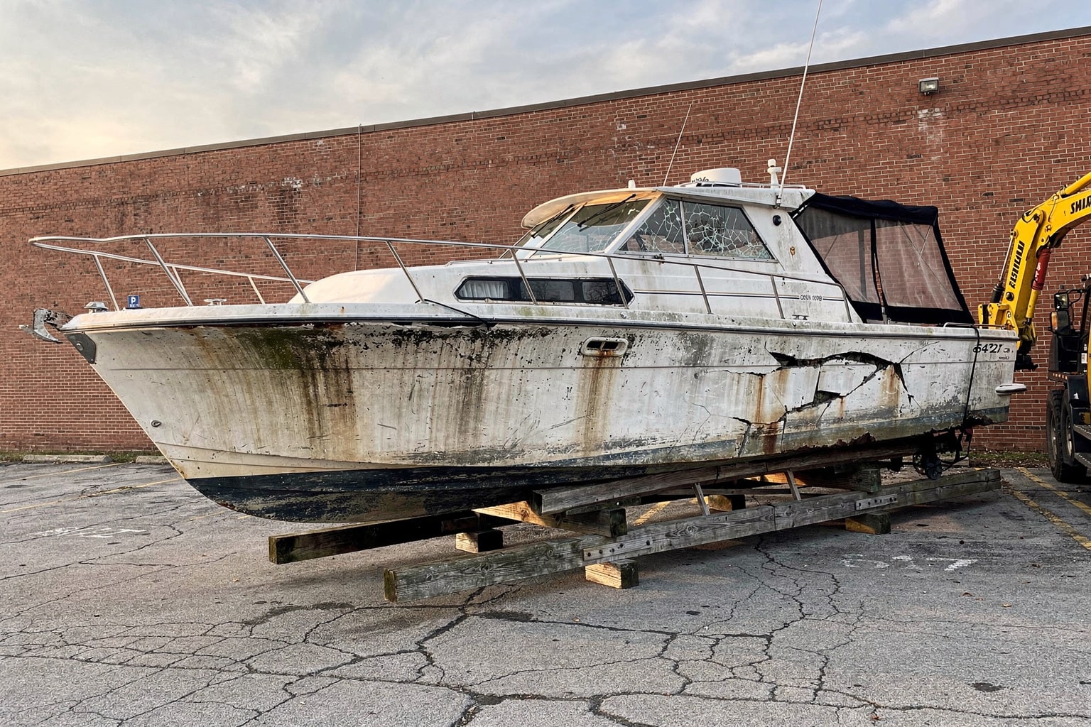 Junk boat removal Indianapolis warehouse lot shows damaged cabin cruiser on cradles ready for disposal