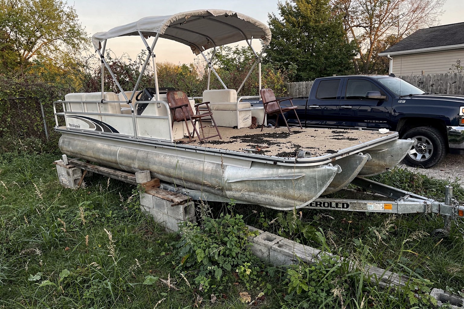 Junk boat removal Indianapolis shows neglected pontoon boat in overgrown yard ready for disposal