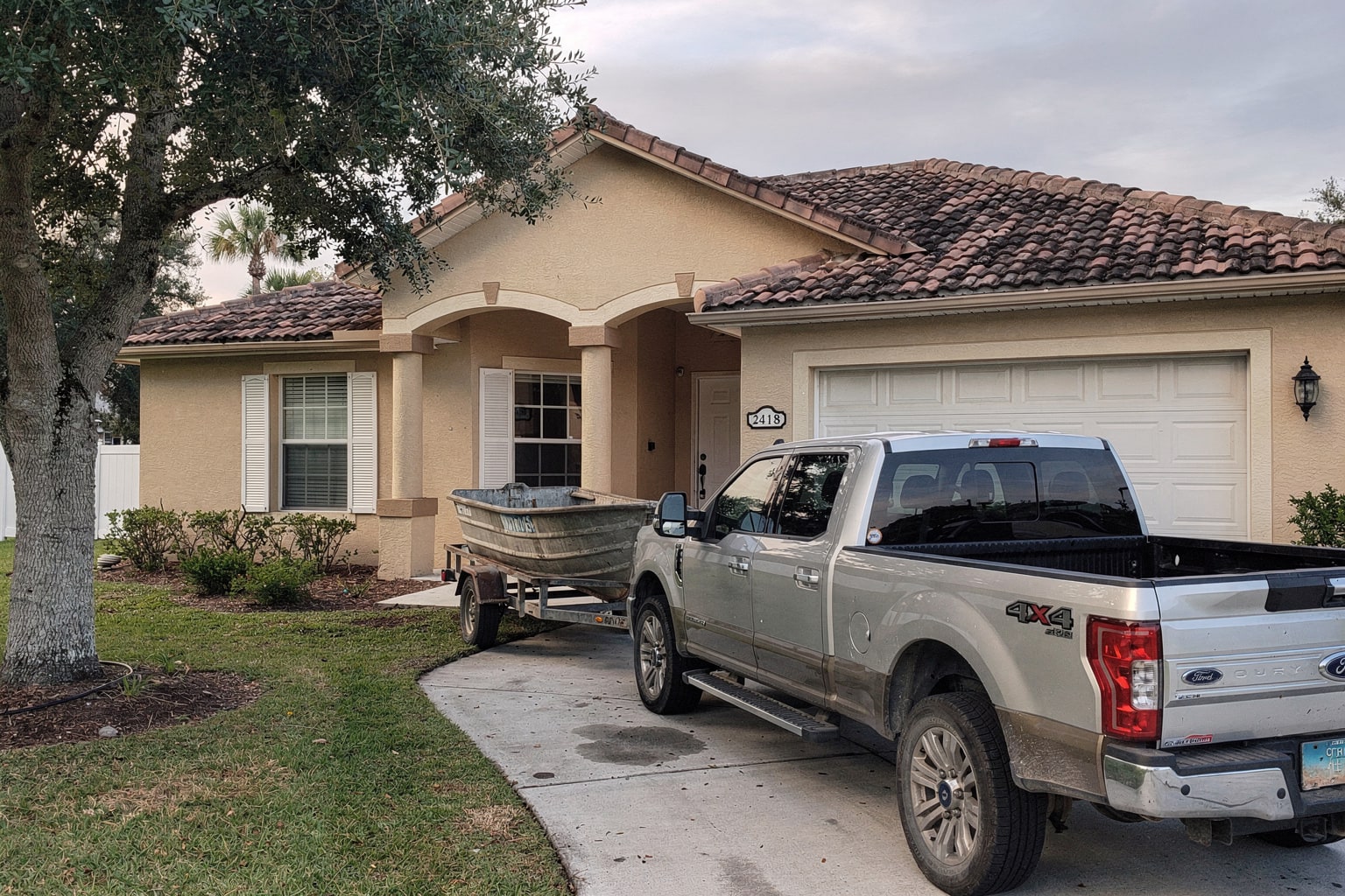 Junk boat removal Jacksonville Florida, silver pickup truck with old aluminum fishing boat on trailer in residential driveway