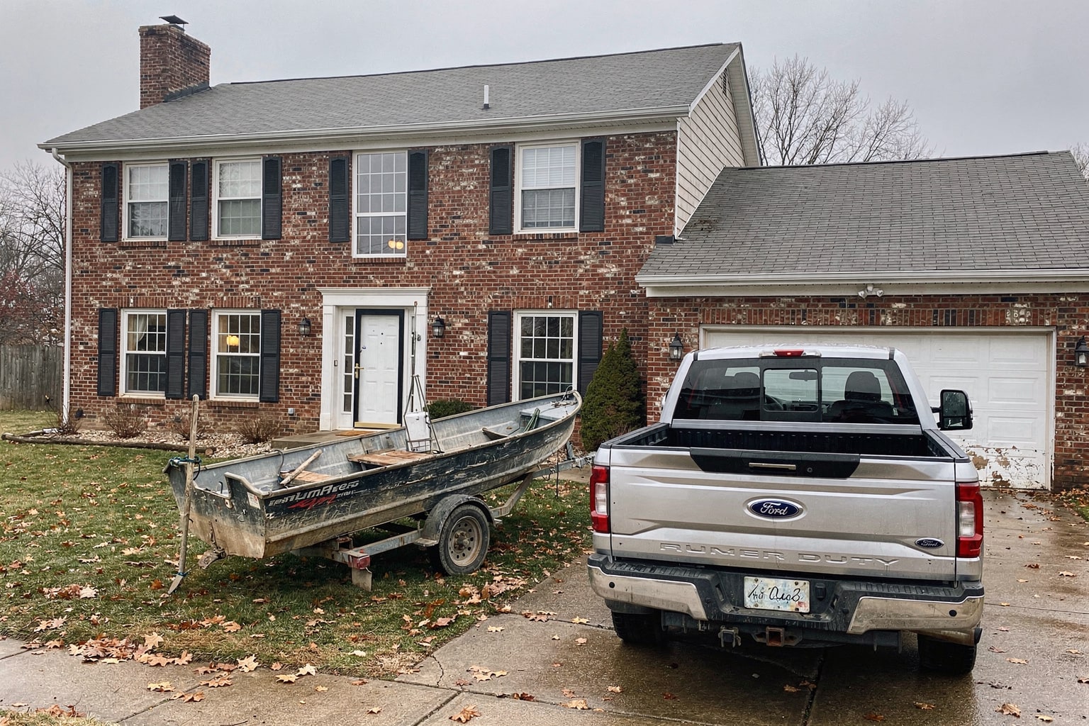 Junk boat removal in Kansas City showing weathered fishing boat loaded on pickup truck trailer in residential driveway