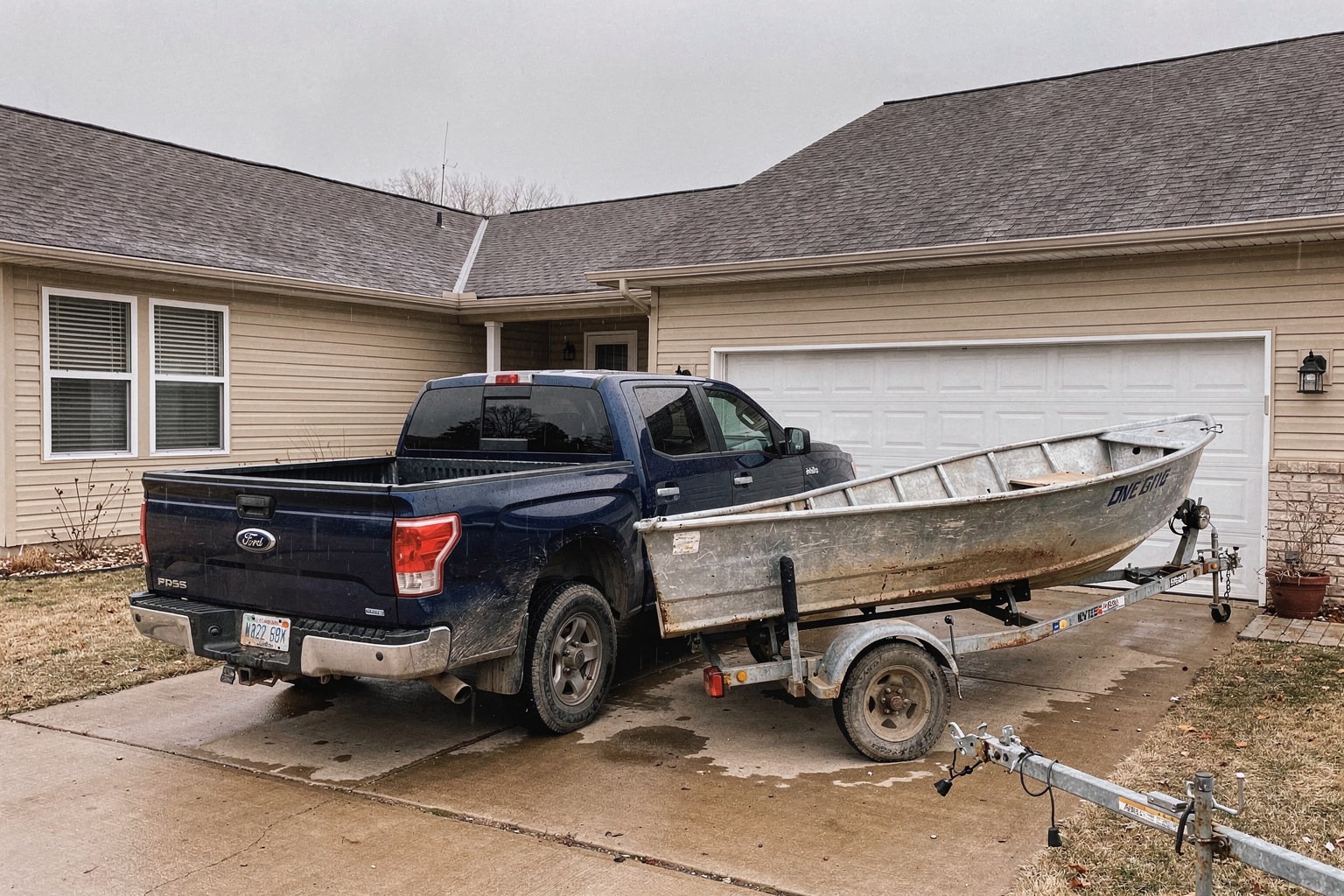 Weathered aluminum fishing boat on trailer hitched to pickup truck in Kansas driveway for junk boat removal