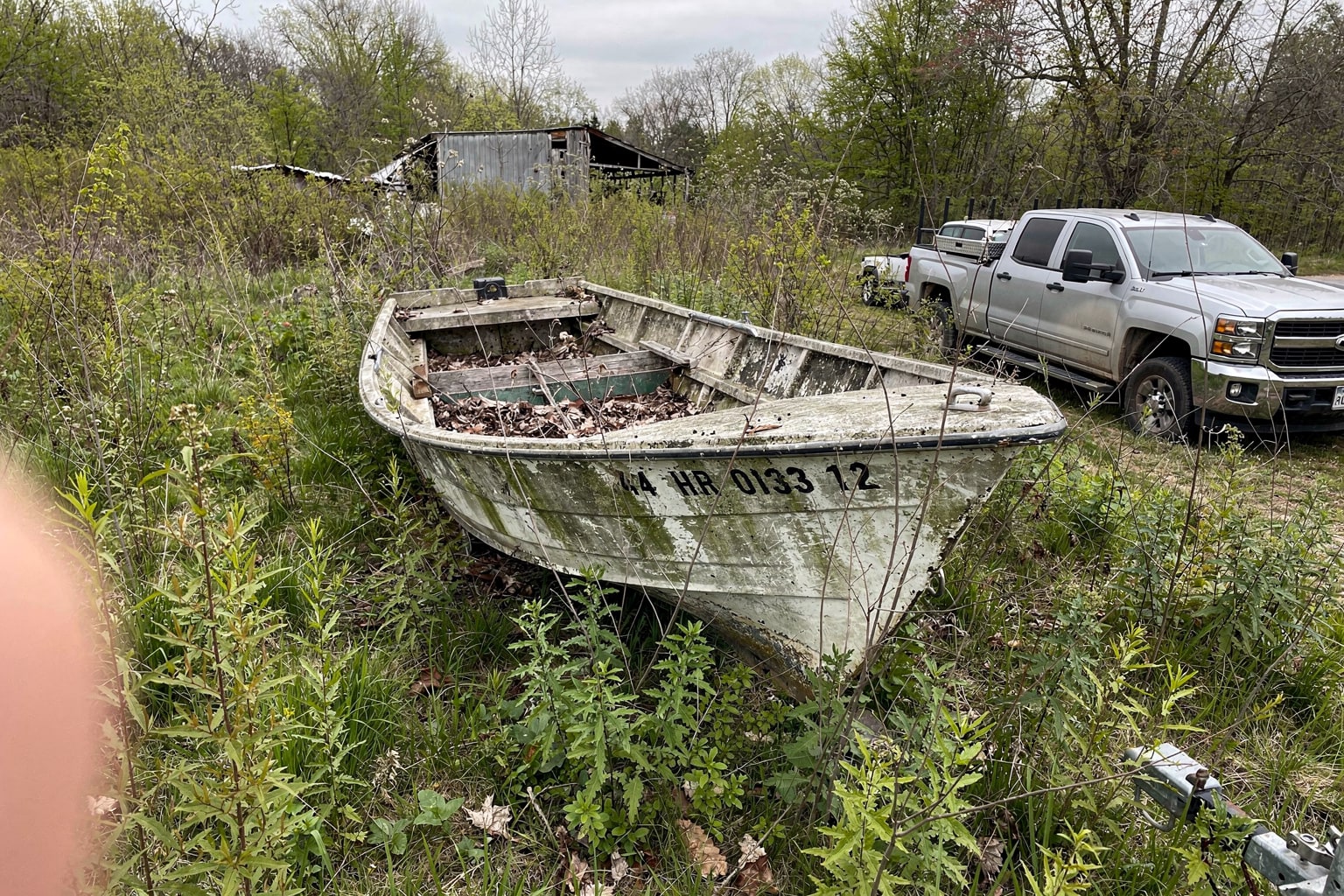 Junk boat salvage Kentucky: deteriorated 18-foot fiberglass boat abandoned in overgrown backyard with removal truck staged nearby