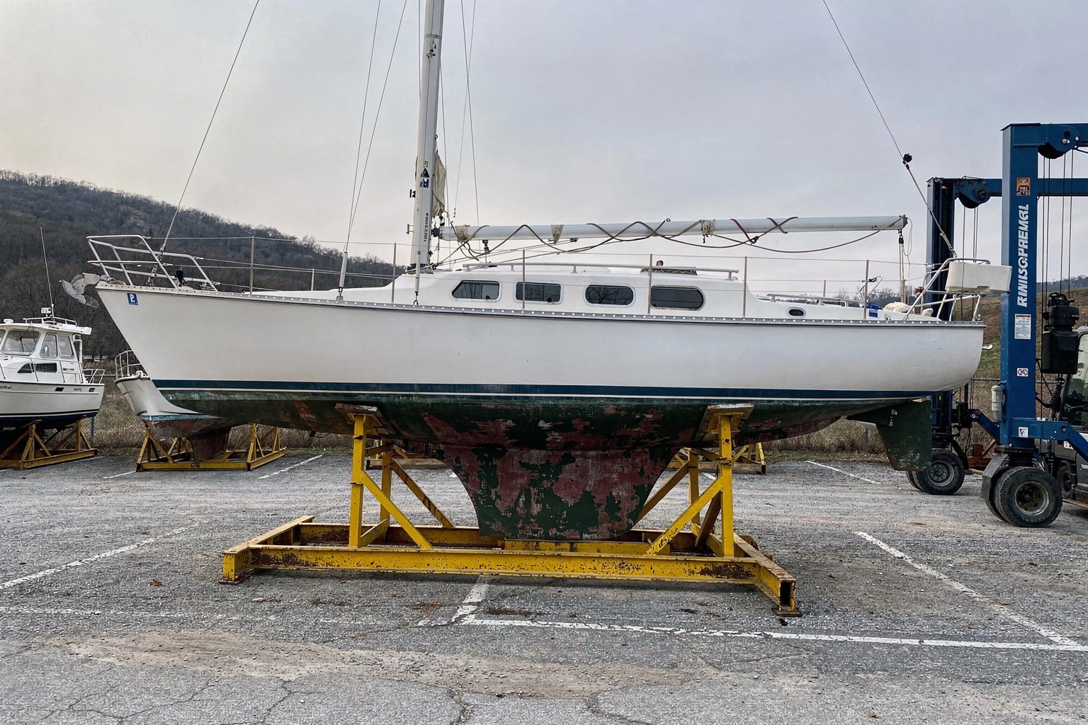 Boat salvage Kentucky boatyard: 28-foot cruising sailboat on steel cradle in dry storage with travel-lift and other vessels visible