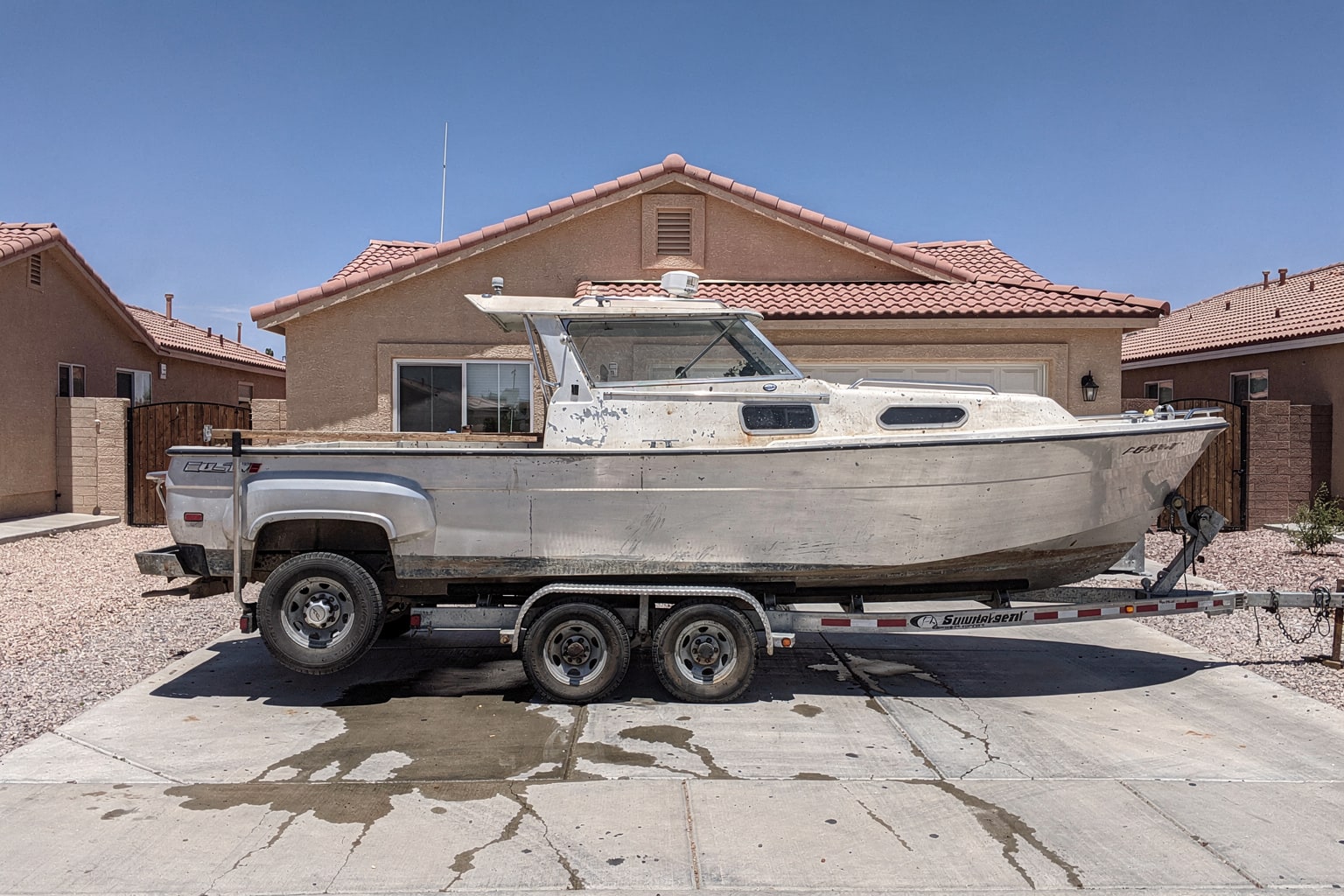 Junk boat removal in Las Vegas — weathered cabin cruiser loaded on pickup truck trailer in residential driveway
