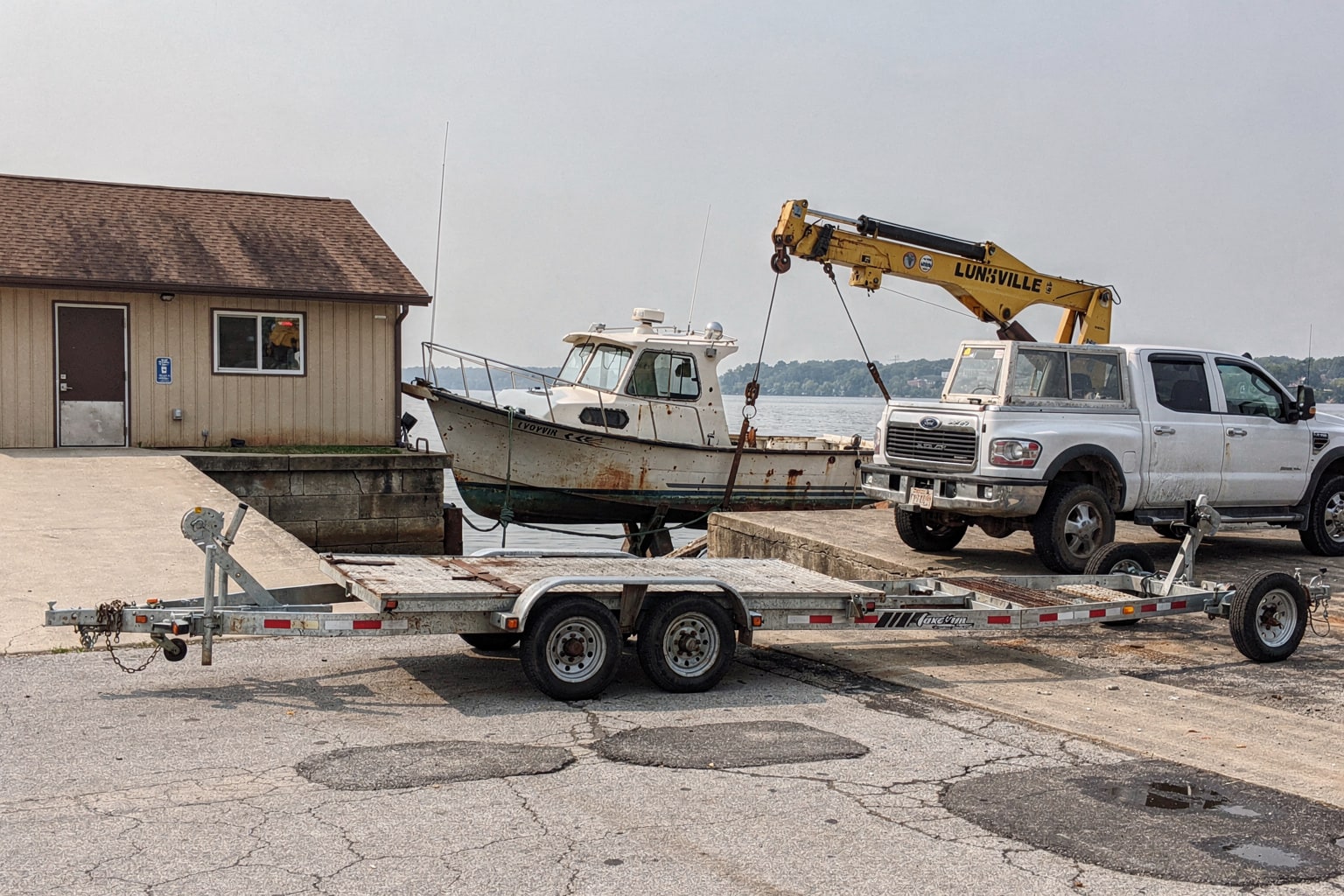 Neglected cabin cruiser at Louisville Kentucky boat launch with hydraulic crane positioned for junk boat removal and disposal