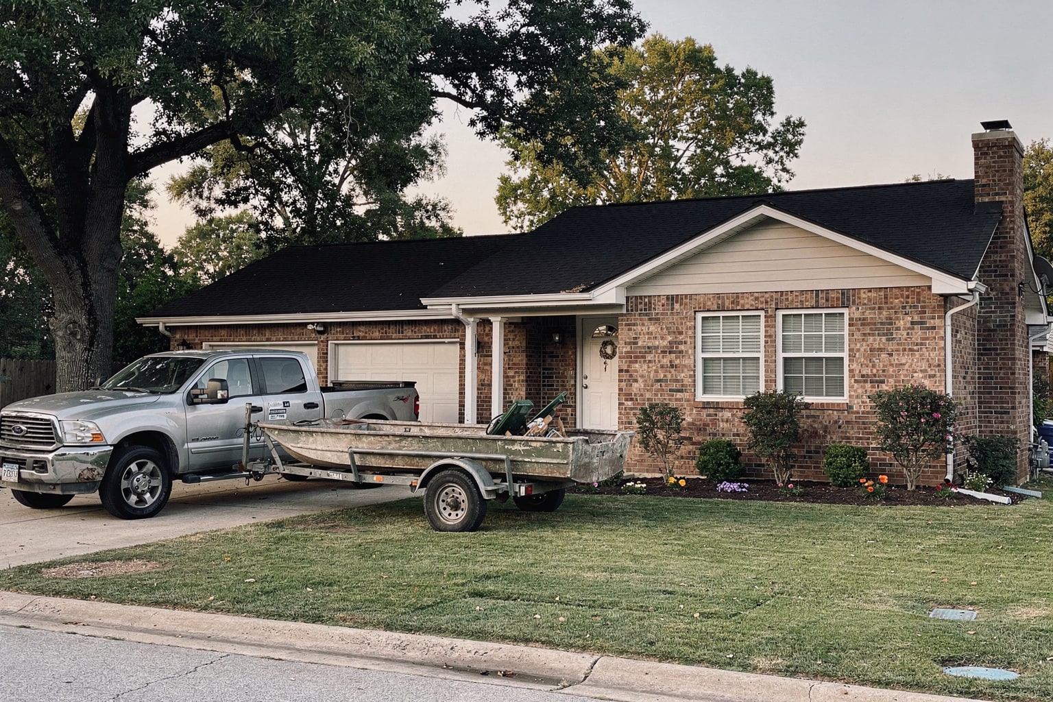 Old aluminum fishing boat loaded on trailer attached to silver pickup truck in Louisville Kentucky residential driveway ready for junk boat removal