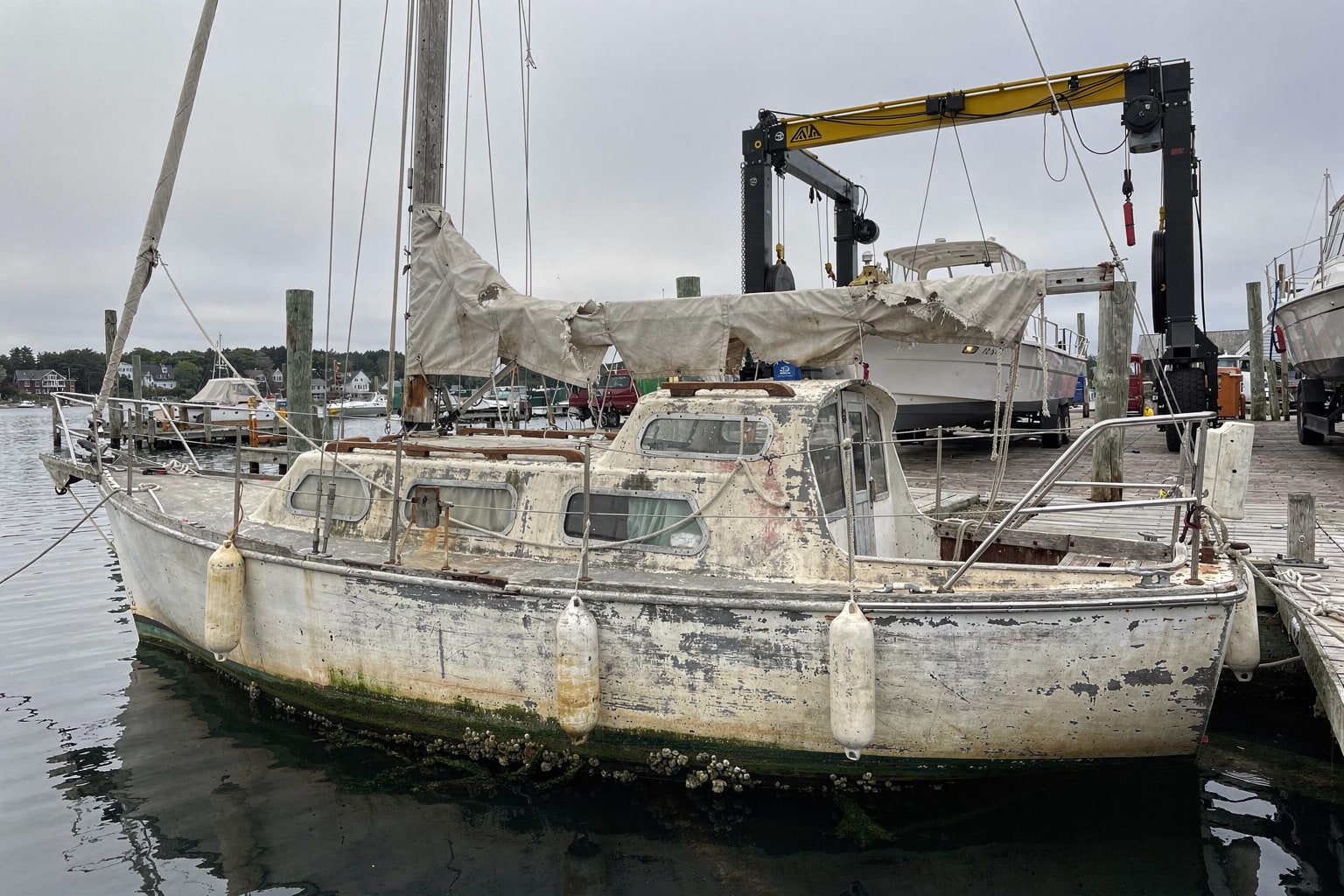 Abandoned 26-foot sailboat with mast down moored at neglected Maine marina dock awaiting removal