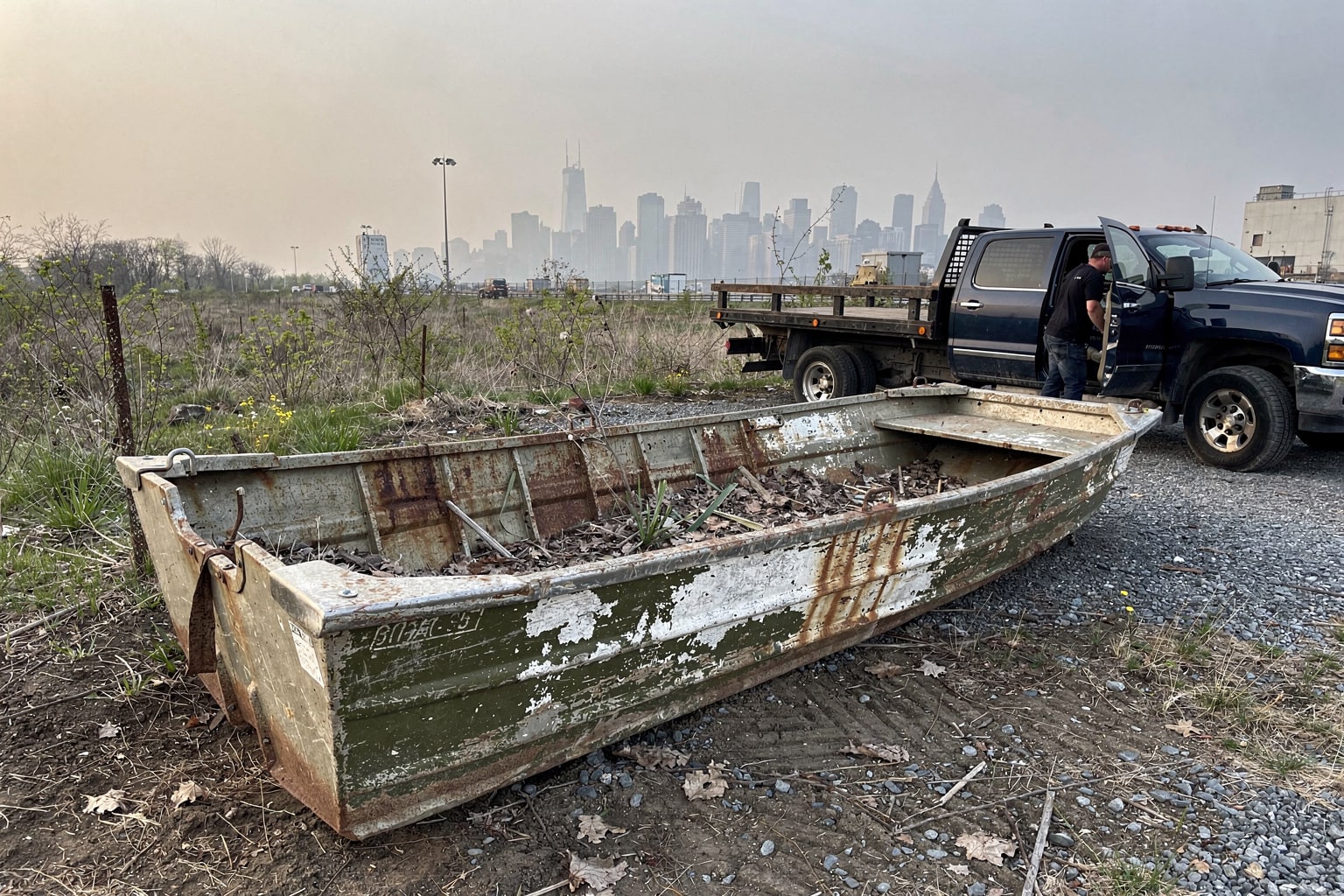 Abandoned junk boat removal from NYC waterfront lot, deteriorated aluminum boat with removal truck approaching