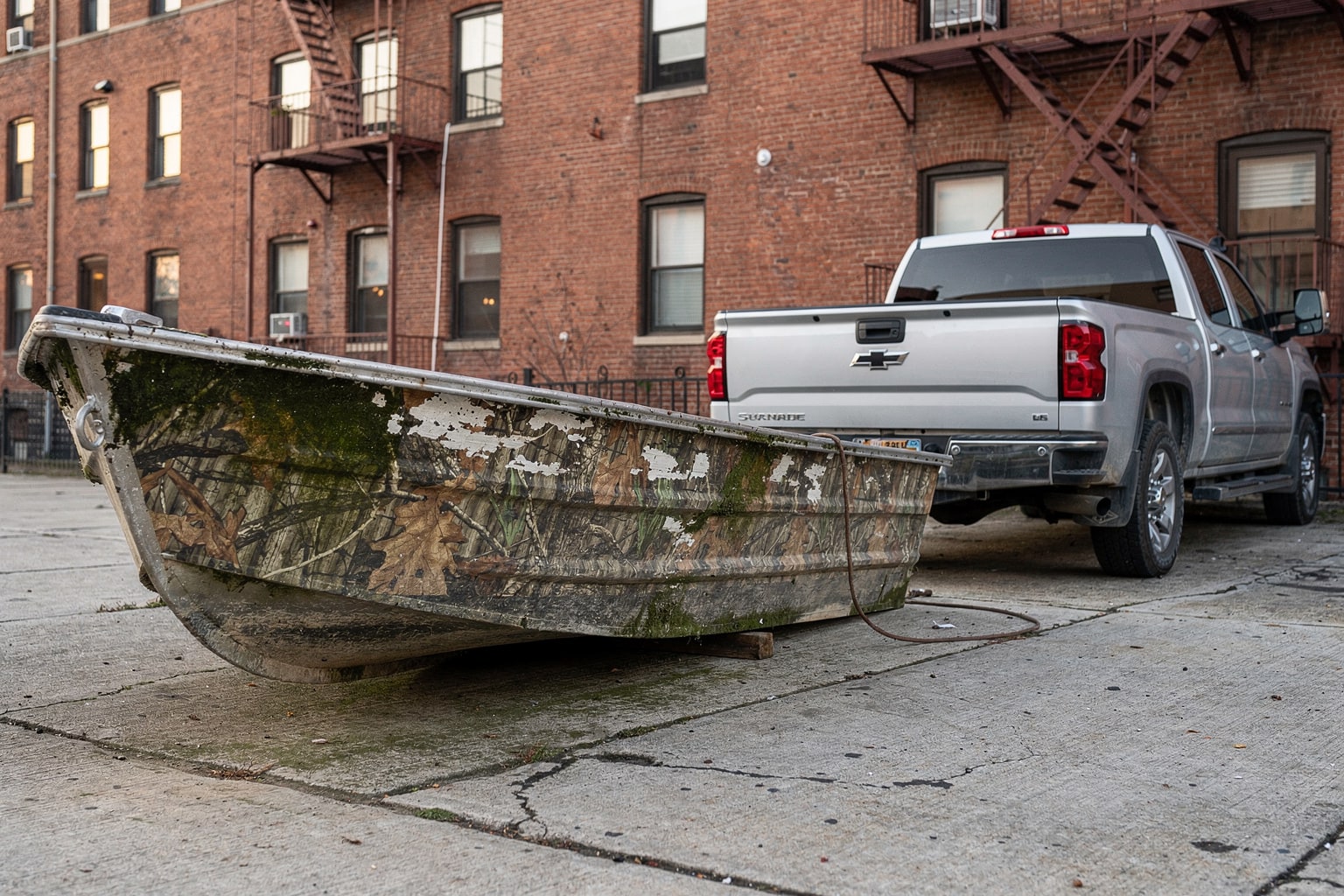 Abandoned weathered aluminum jon boat on Manhattan loading dock surrounded by junk and debris, removal truck approaching