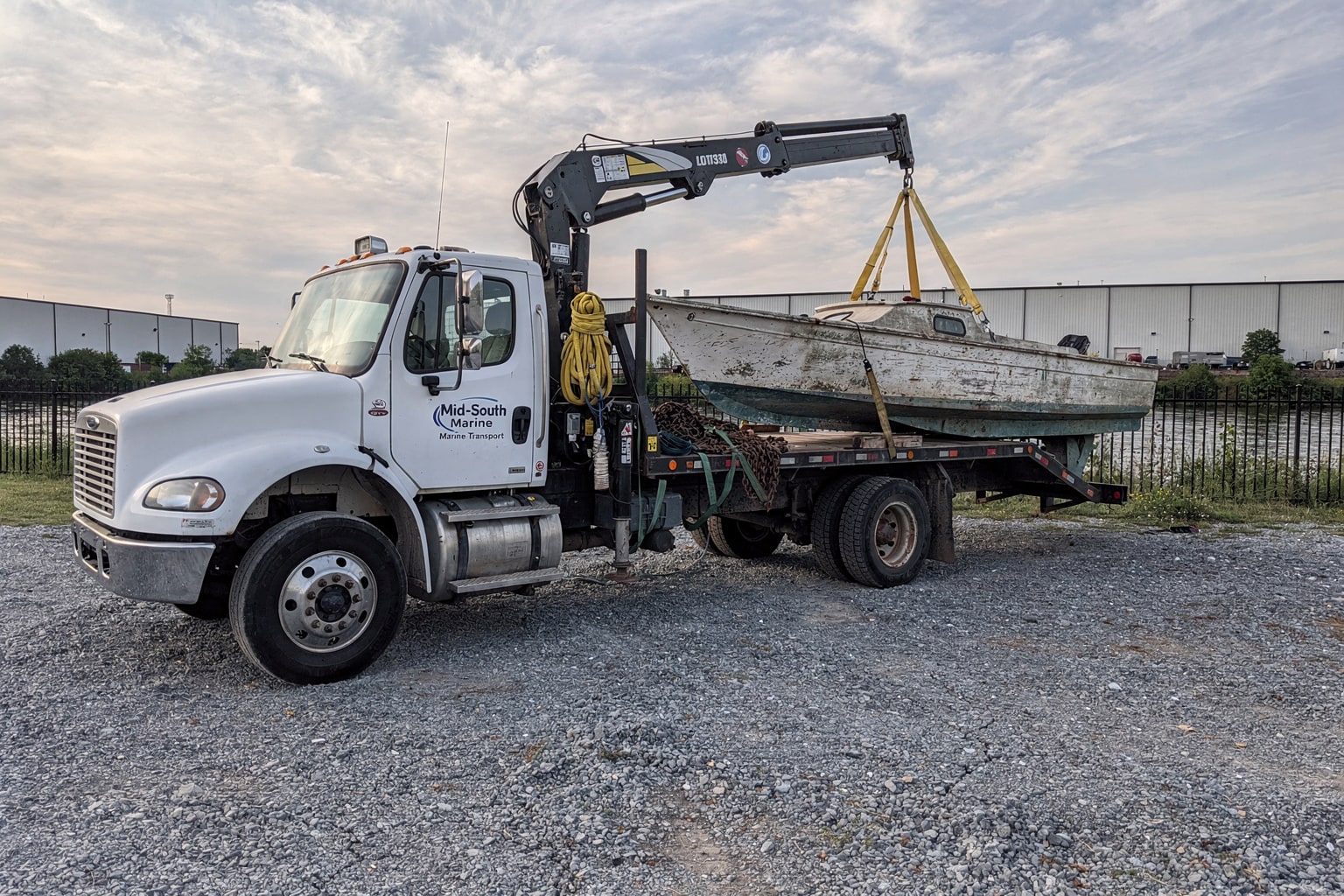 Commercial flatbed truck and crane removing large junk sailboat from Memphis riverside lot