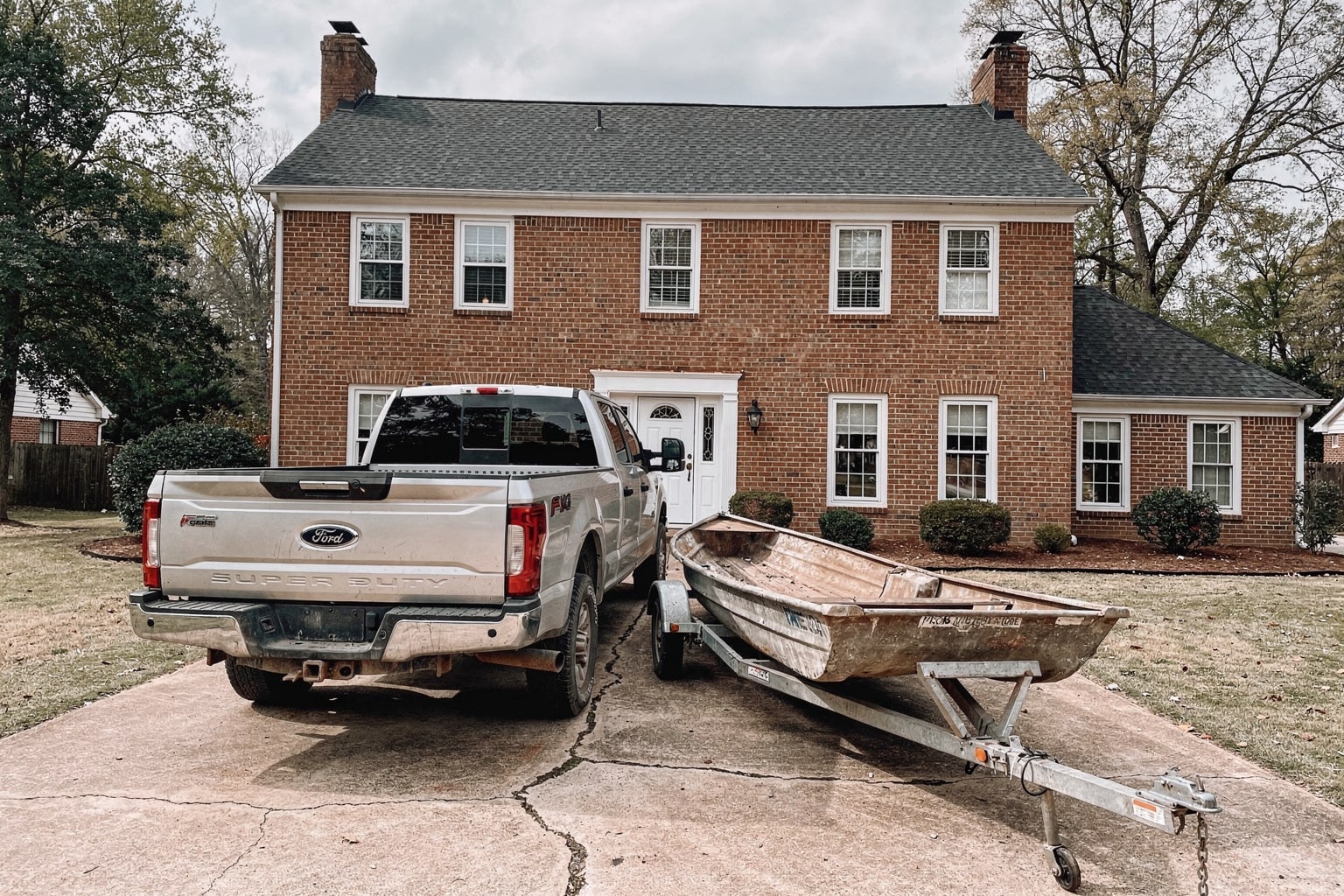 Silver pickup truck with boat trailer removing junk boat from Memphis driveway