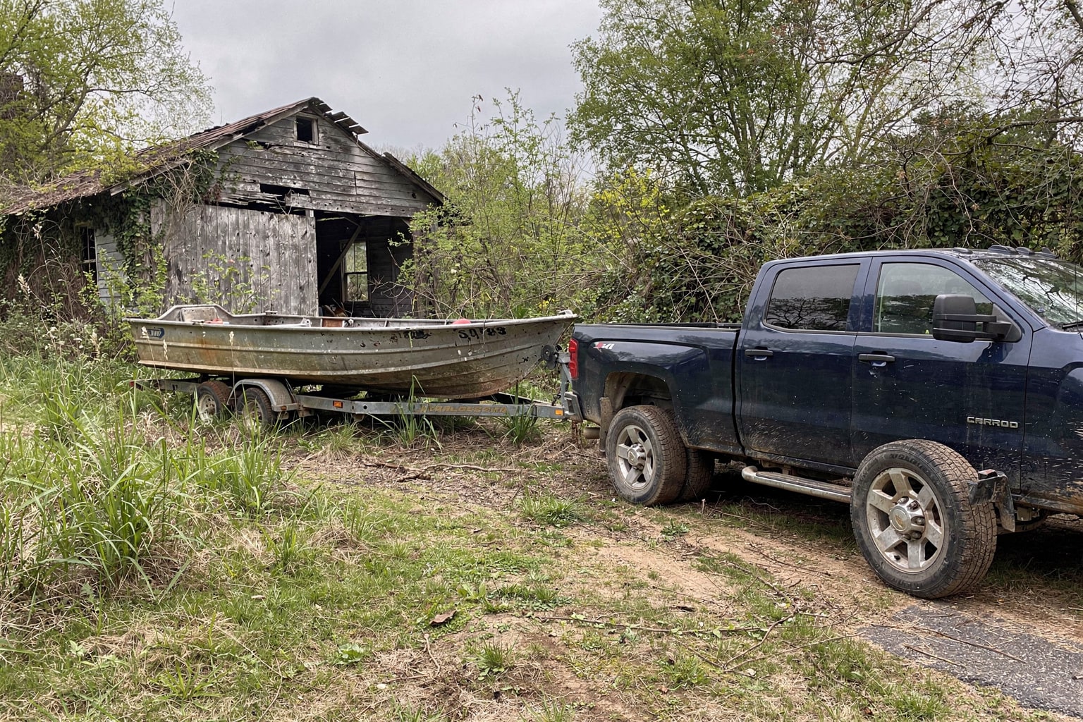Chevy truck and trailer preparing to haul deteriorated junk boat from overgrown Memphis yard