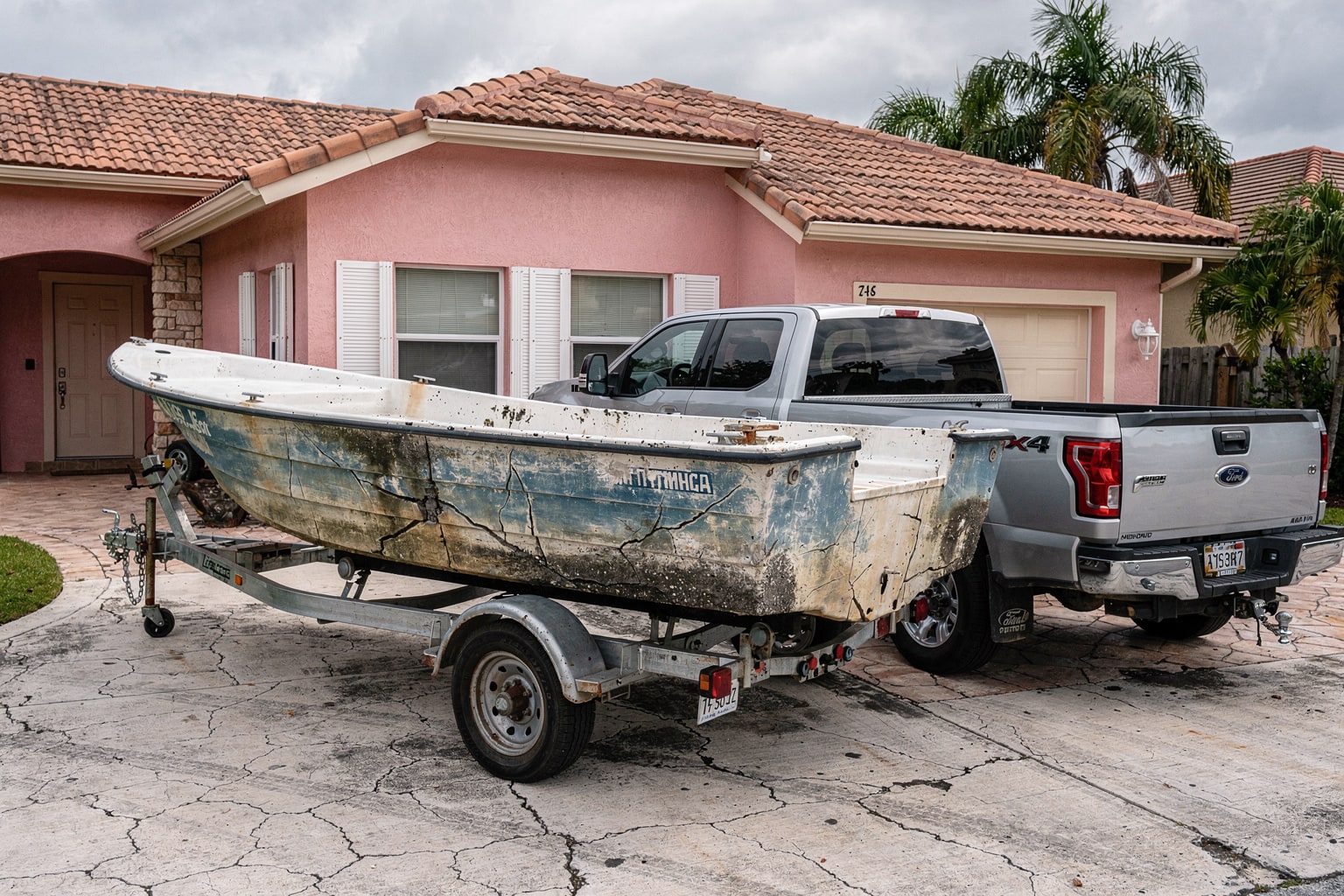 Junk boat removal Miami FL silver pickup truck trailer with weathered 20-foot powerboat loaded lengthwise ready for disposal